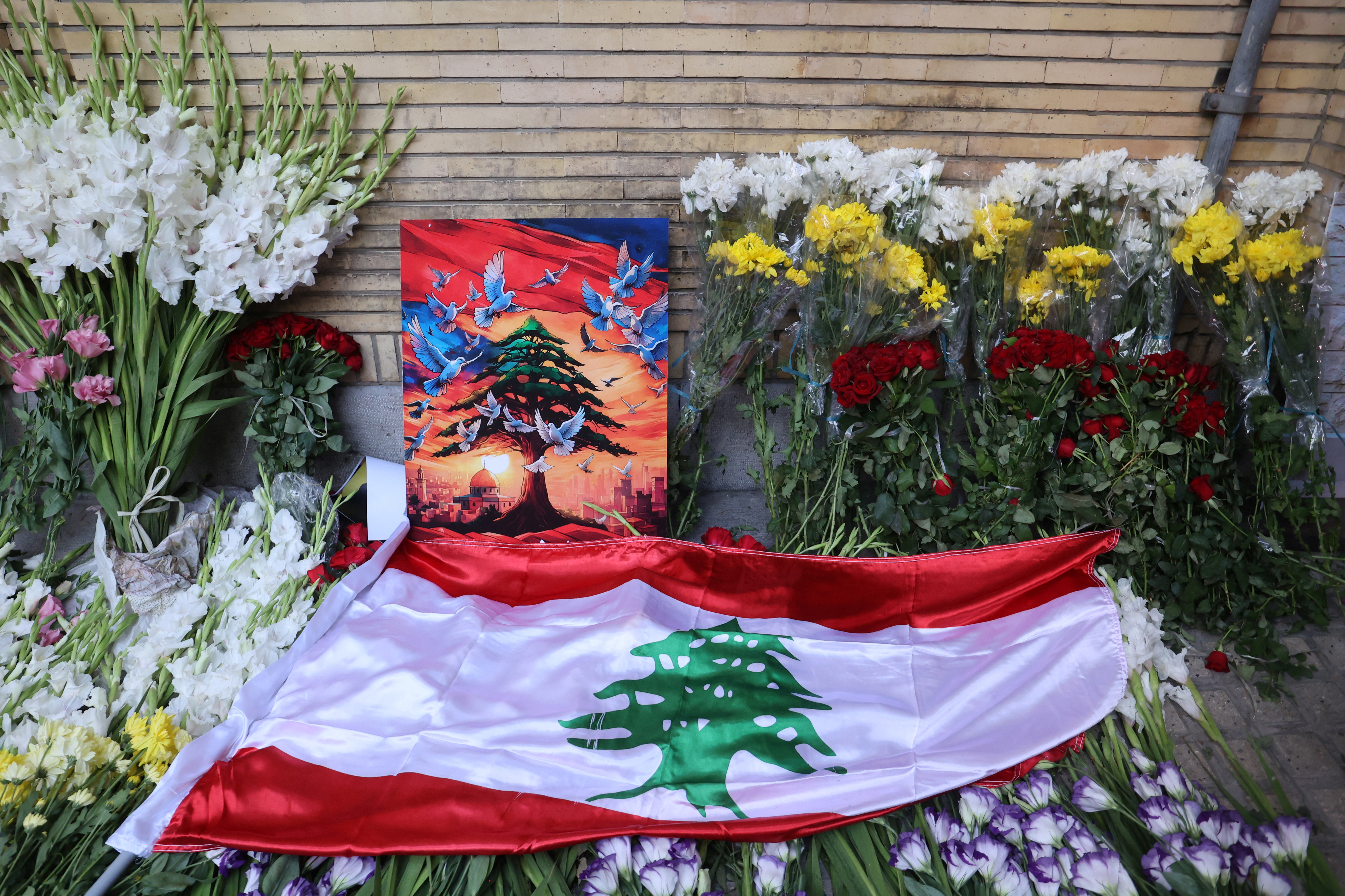 The Lebanese Flag is displayed among the flowers at the gate of Lebanon's Embassy of Iran following the explosion of pagers across Lebanon, in Tehran