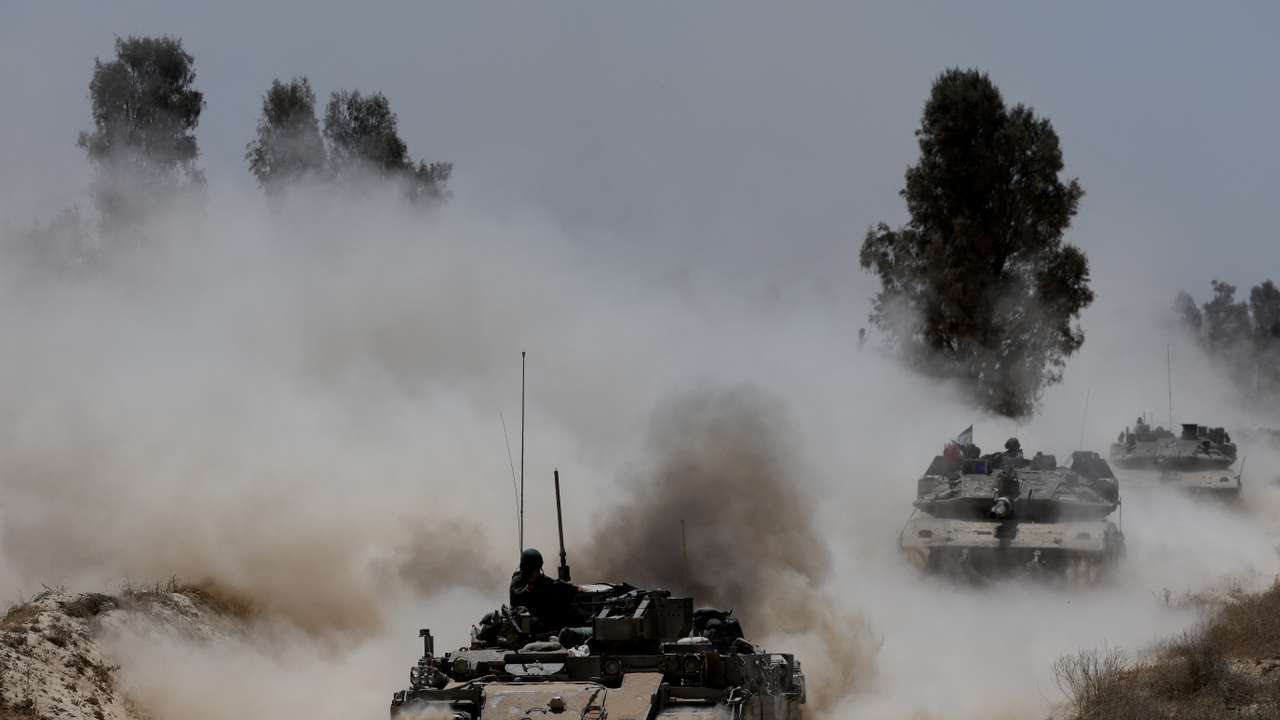 Military vehicles drive their way from the Israeli side of the Israel-Gaza border into Gaza