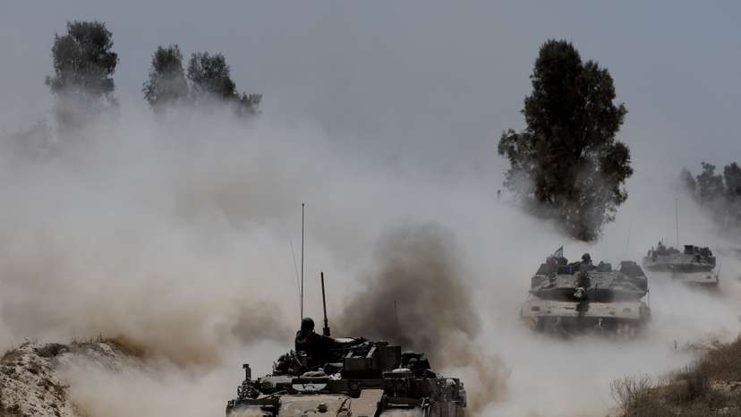 Military vehicles drive their way from the Israeli side of the Israel-Gaza border into Gaza
