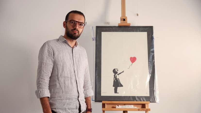 Gallery manager Lindor Mehmetaj poses for a photo next to Banksy's 'Girl with Balloon', in London