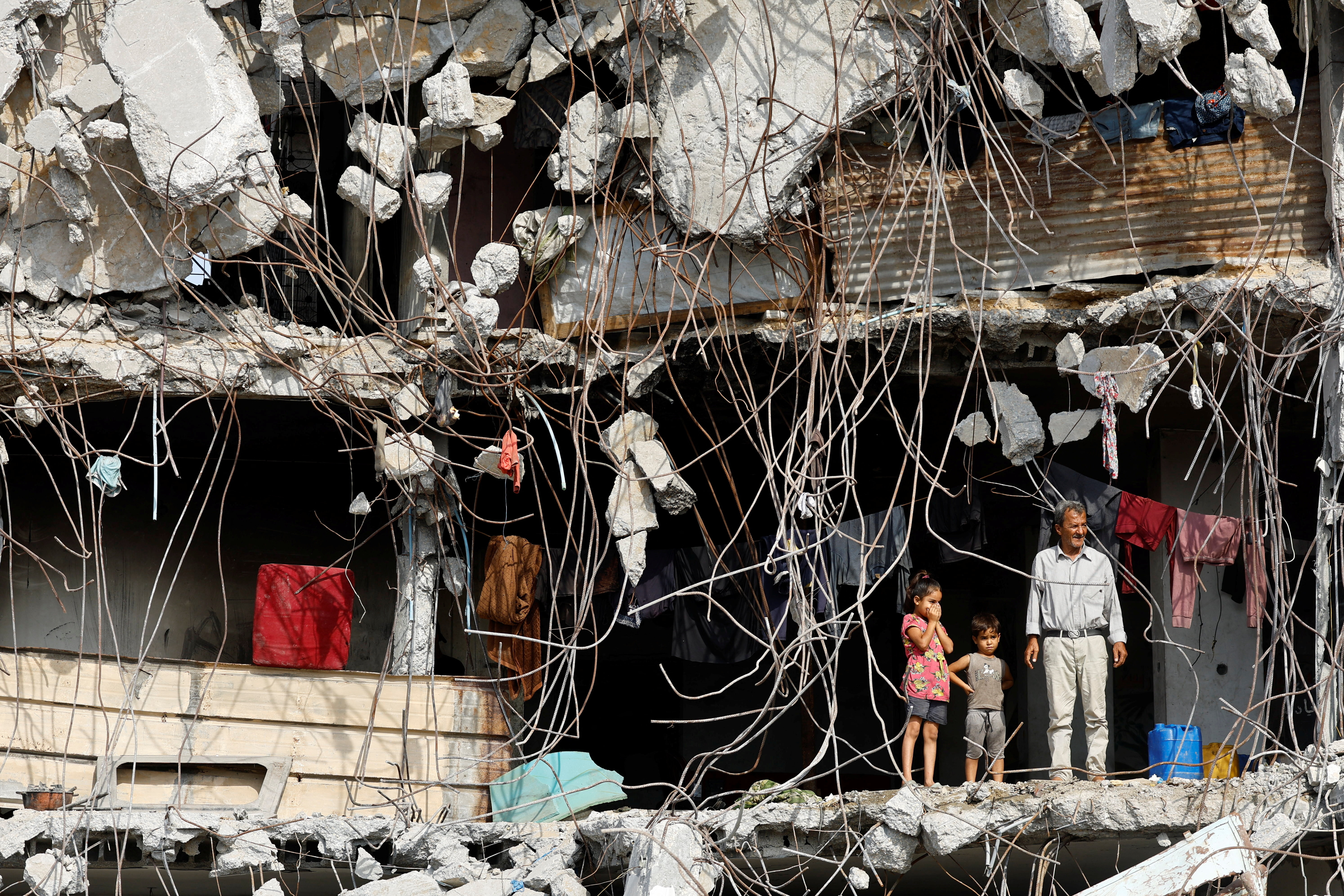 A Palestinian man and children stand at a heavily damaged building surrounded by rebar and rubble,  amid a ceasefire between Israel and Hamas, in Gaza City