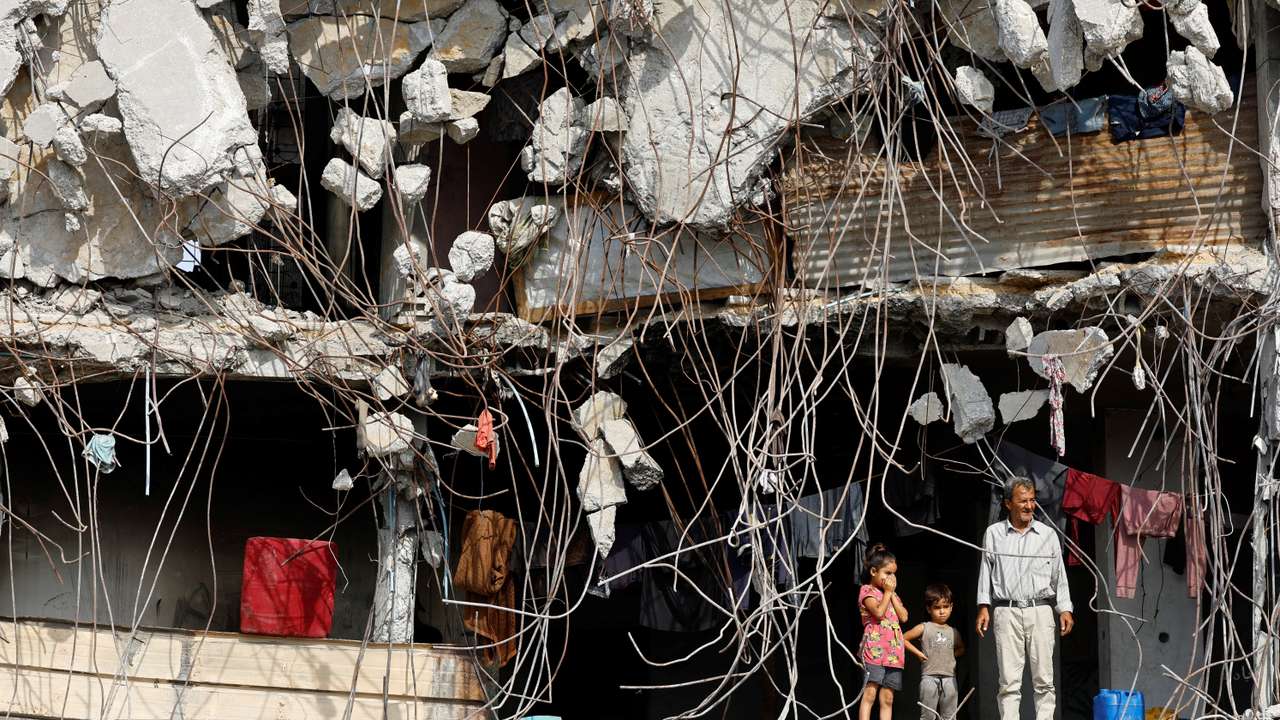 A Palestinian man and children stand at a heavily damaged building surrounded by rebar and rubble, amid a ceasefire between Israel and Hamas, in Gaza City