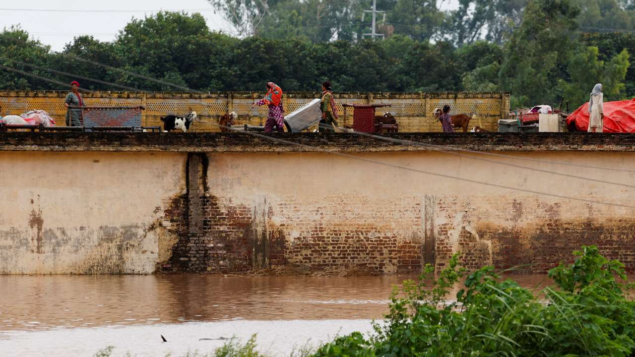 A family with their belongings takes refuge over a roof of their house near Chenab River, following the monsoon rains and rising water level in Wazirabad