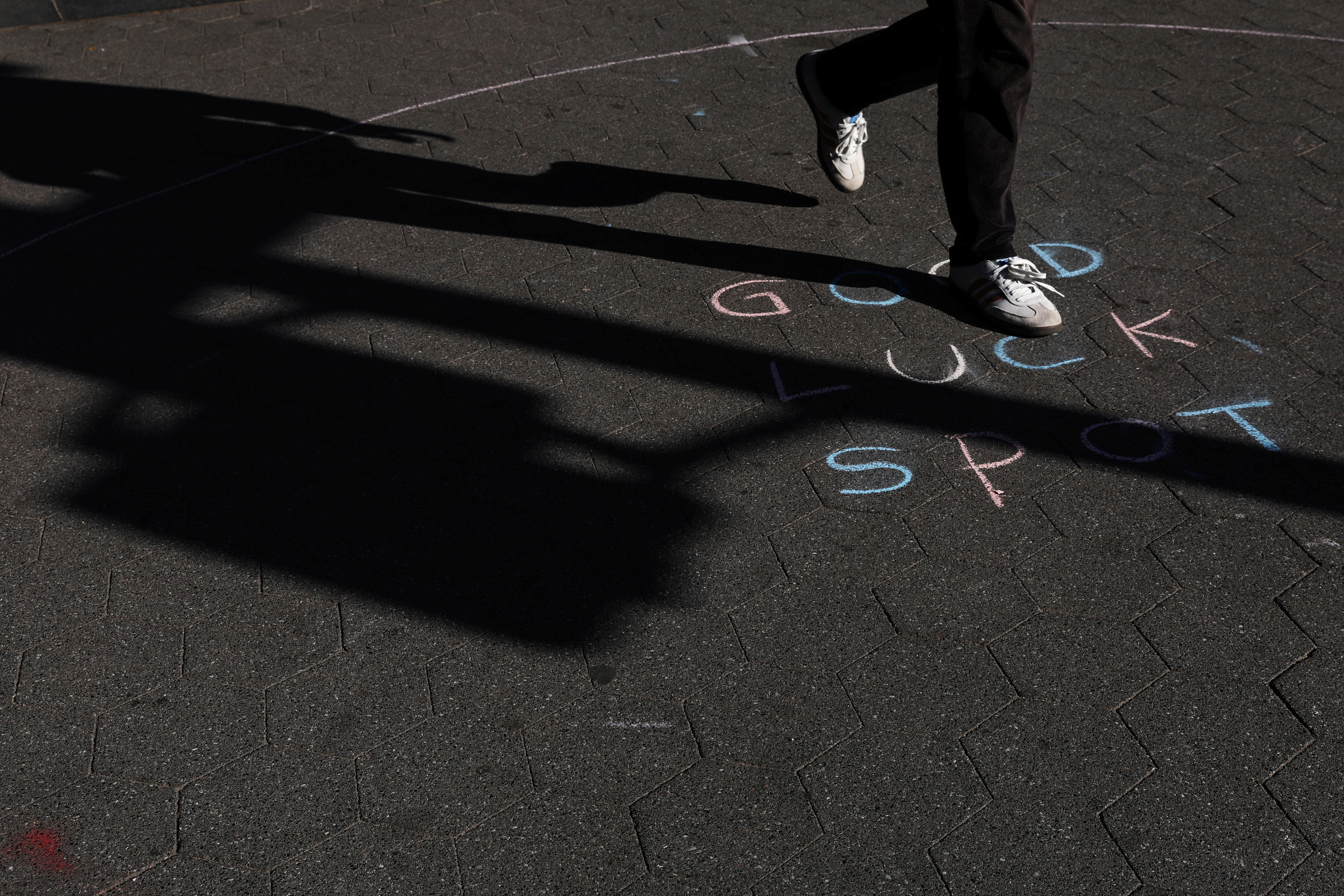 A man walks by a chalked expression on a sidewalk during sunny fall weather at Washington Square Park in New York City