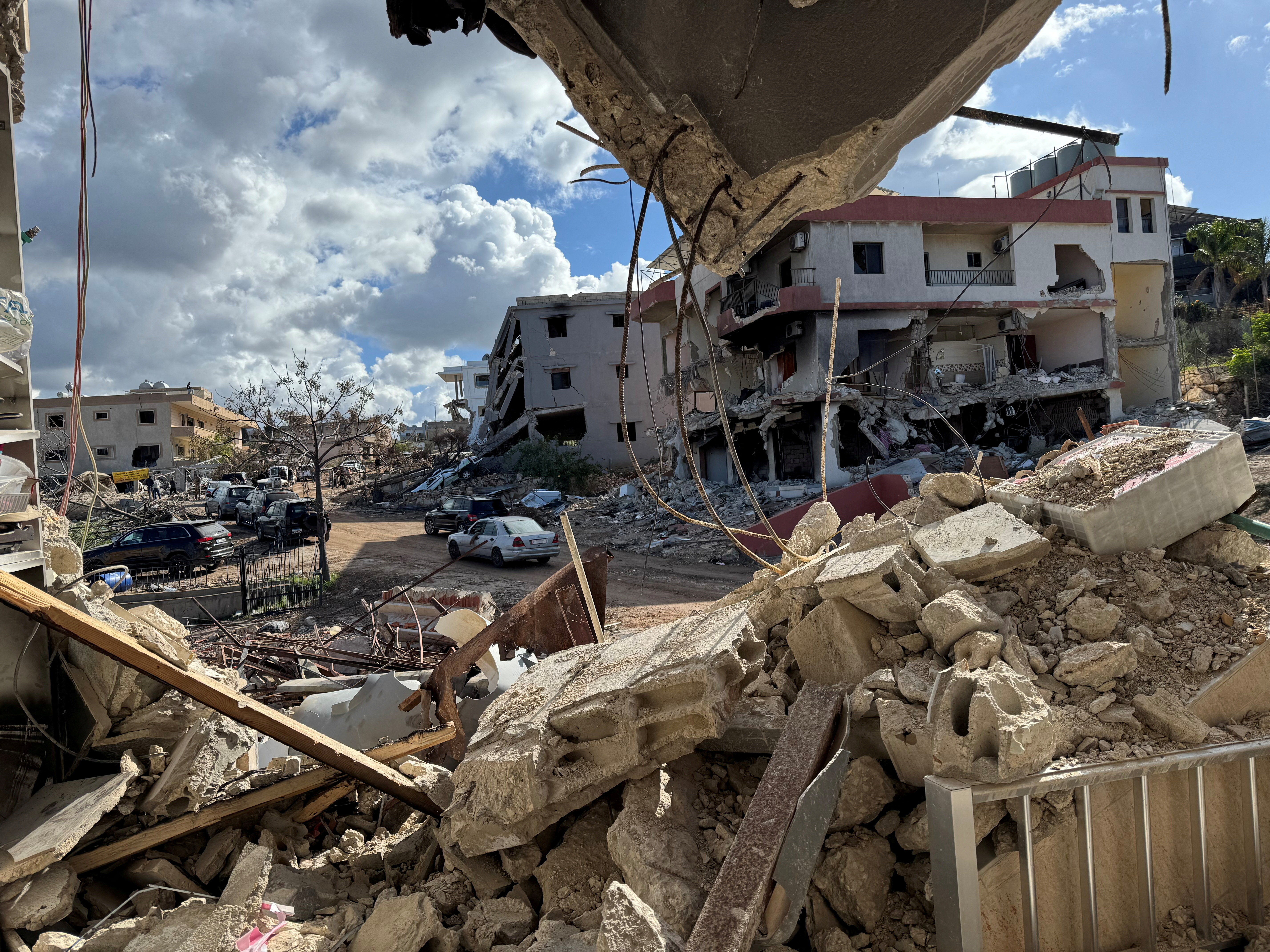 Cars drive past damaged buildings, as residents return to Naqoura