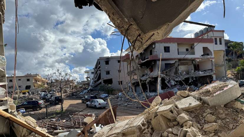 Cars drive past damaged buildings, as residents return to Naqoura