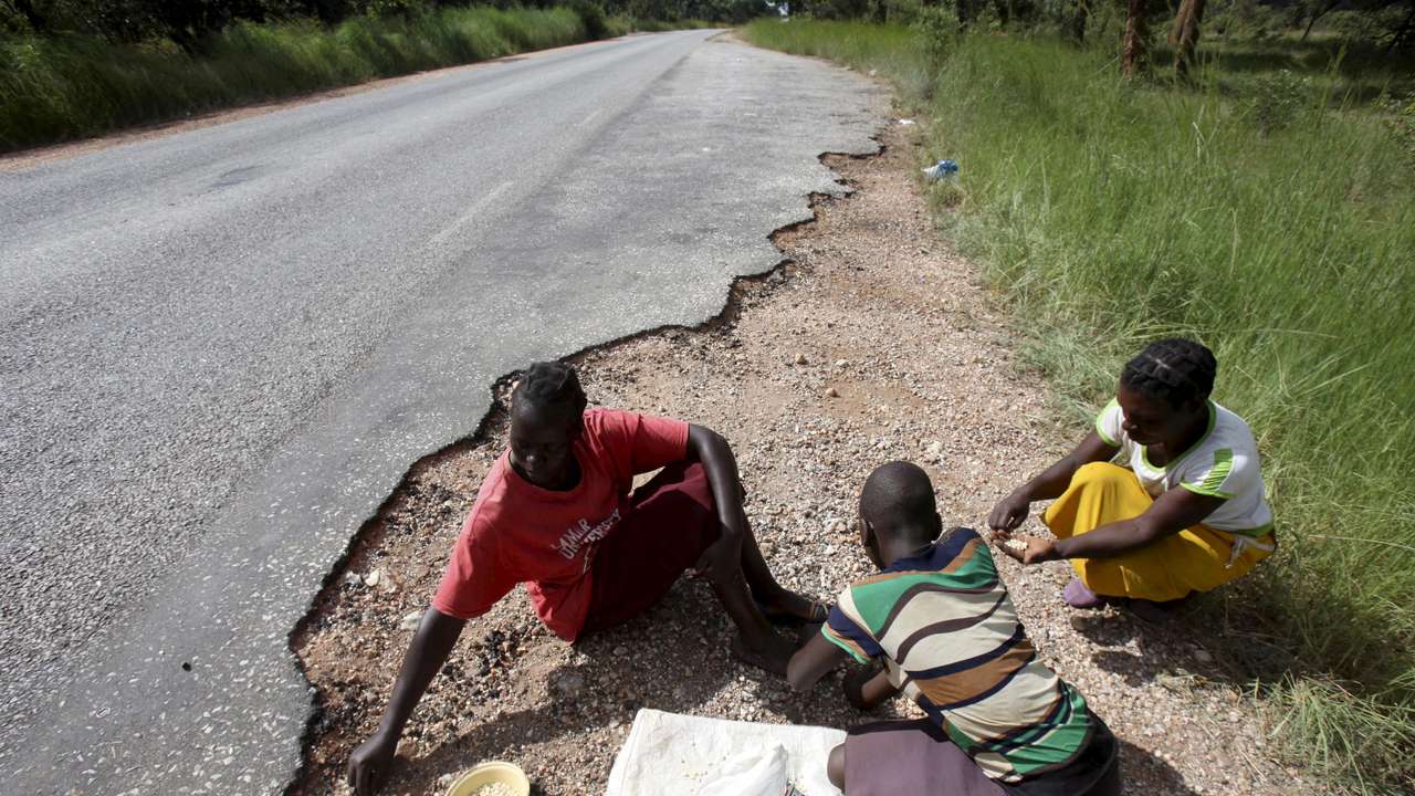 FILE PHOTO: Women gather grain spilled by cargo trucks from Zambia along a highway in Magunje