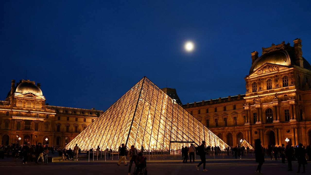 People walk near the glass Pyramid of the Louvre museum