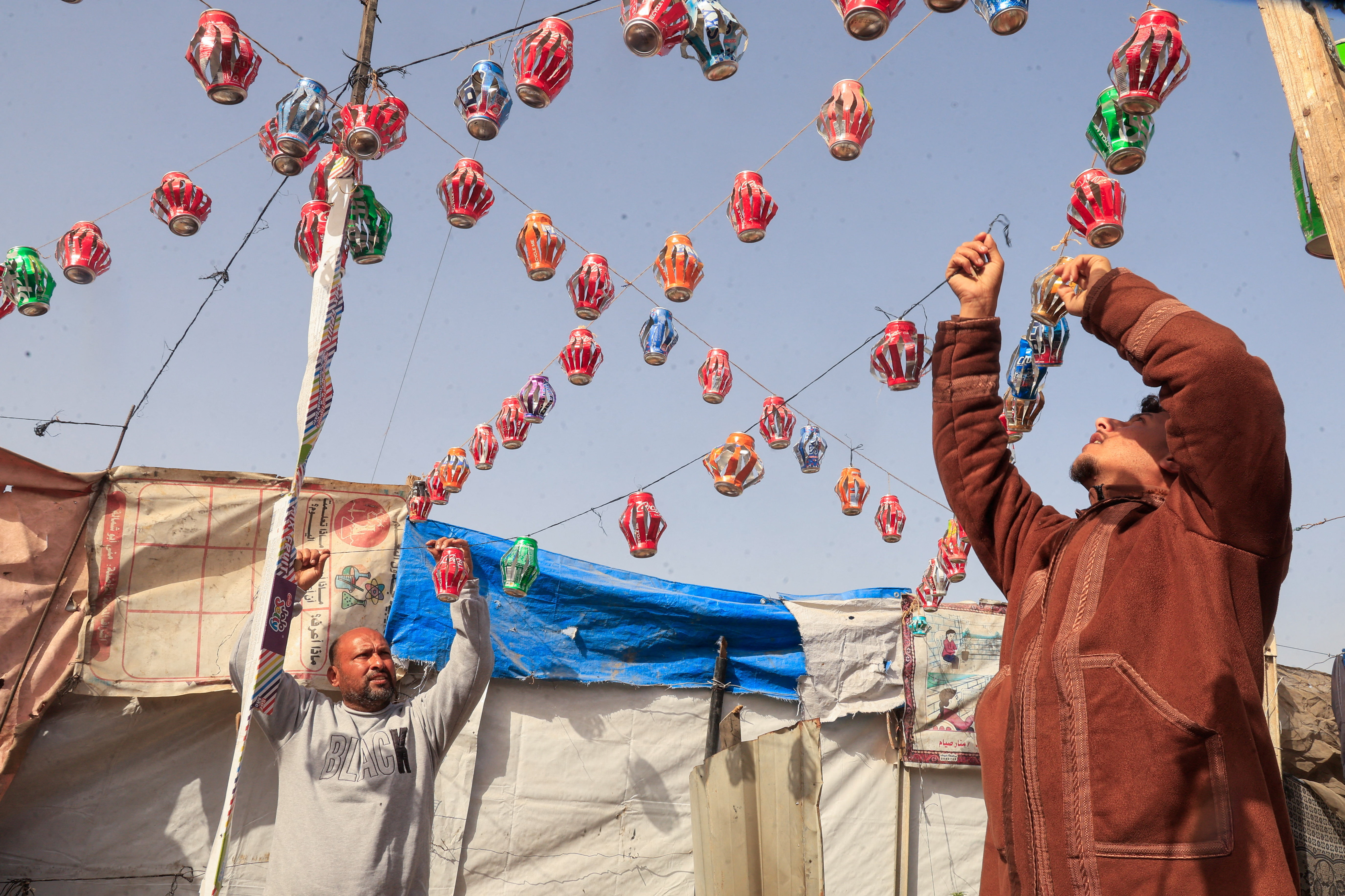Mohannad al-Najjar hangs Ramadan lanterns made from recycled tin cans on strings between tents, in Khan Younis