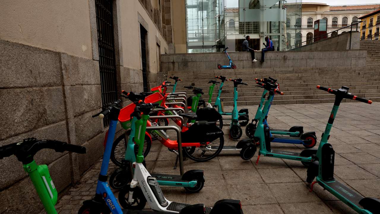 Men speak next to parked e-scooters from Tier, Lime and Dott outside Reina Sofia museum in downtown Madrid
