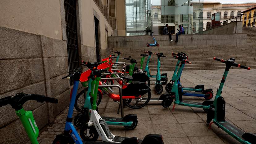 Men speak next to parked e-scooters from Tier, Lime and Dott outside Reina Sofia museum in downtown Madrid