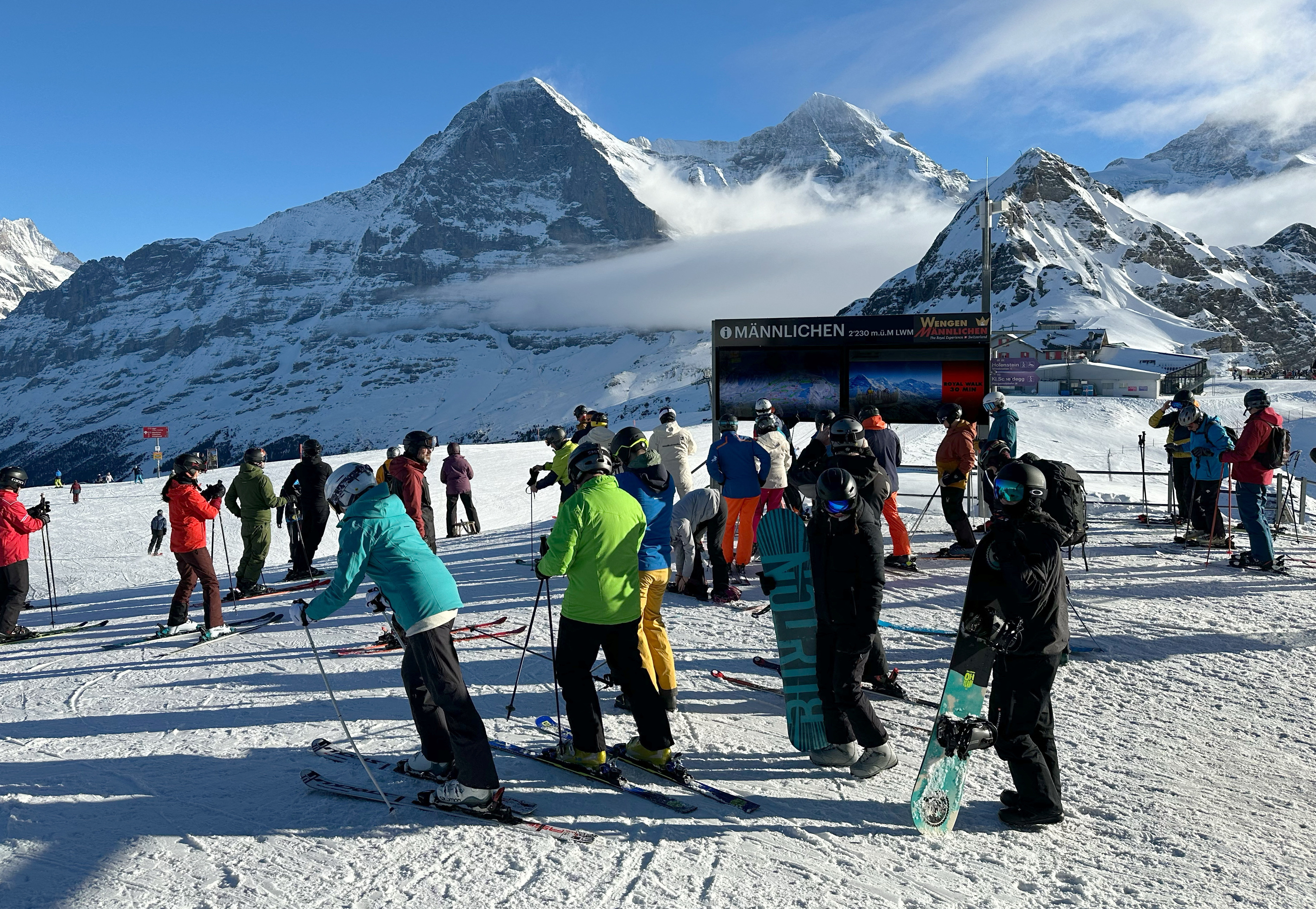 Skiers are pictured near a Mannlichen signboard in front of the Eiger and Monch mountains, in the alpine ski resort of Wengen
