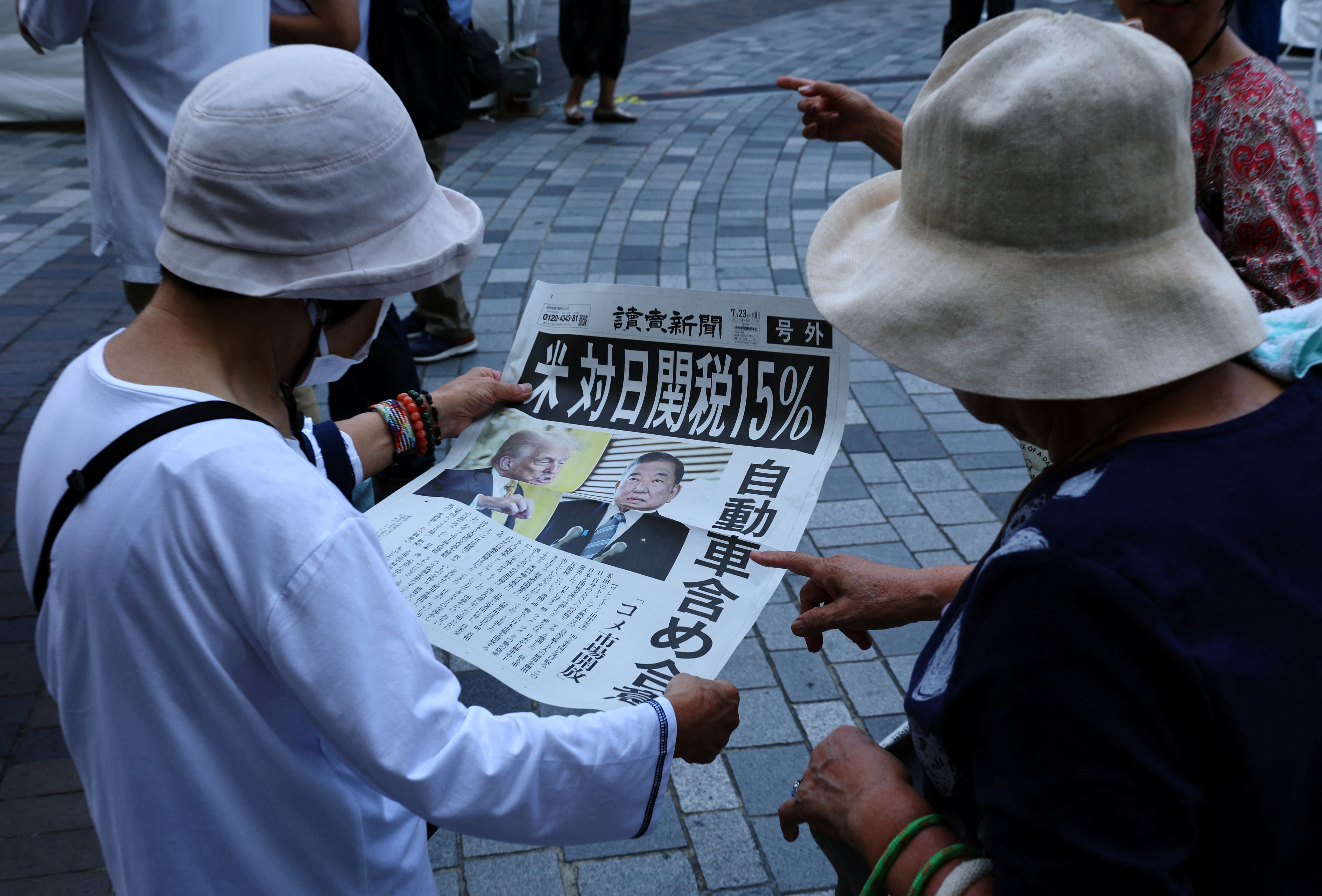 People react as they read a special edition of Yomiuri Shimbun newspaper reporting the tariff deal agreement between U.S and Japan, in Tokyo