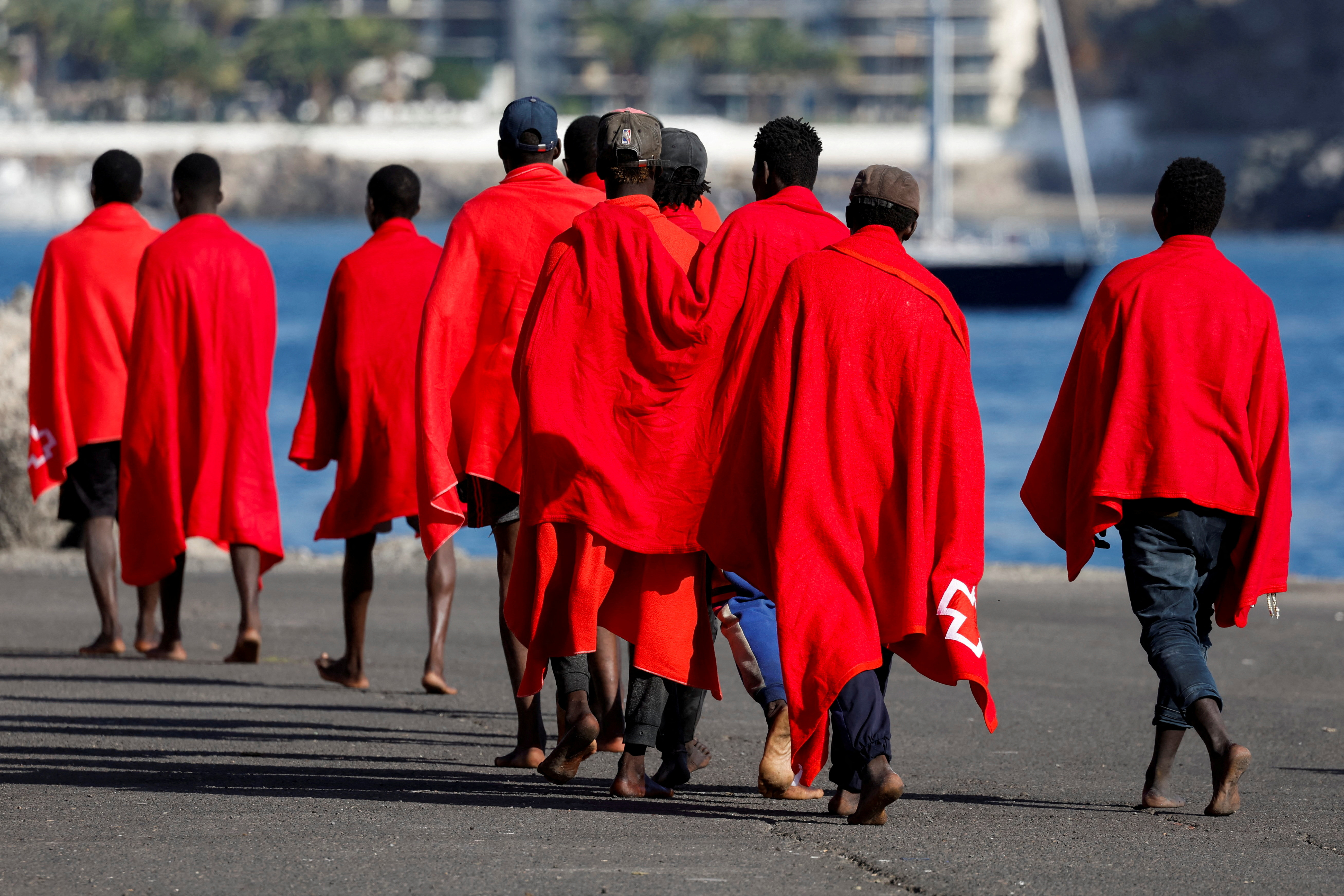 FILE PHOTO: A group of migrants walk in the port of Arguineguin to be assisted by the Red Cross after disembarking from a Spanish coast guard vessel