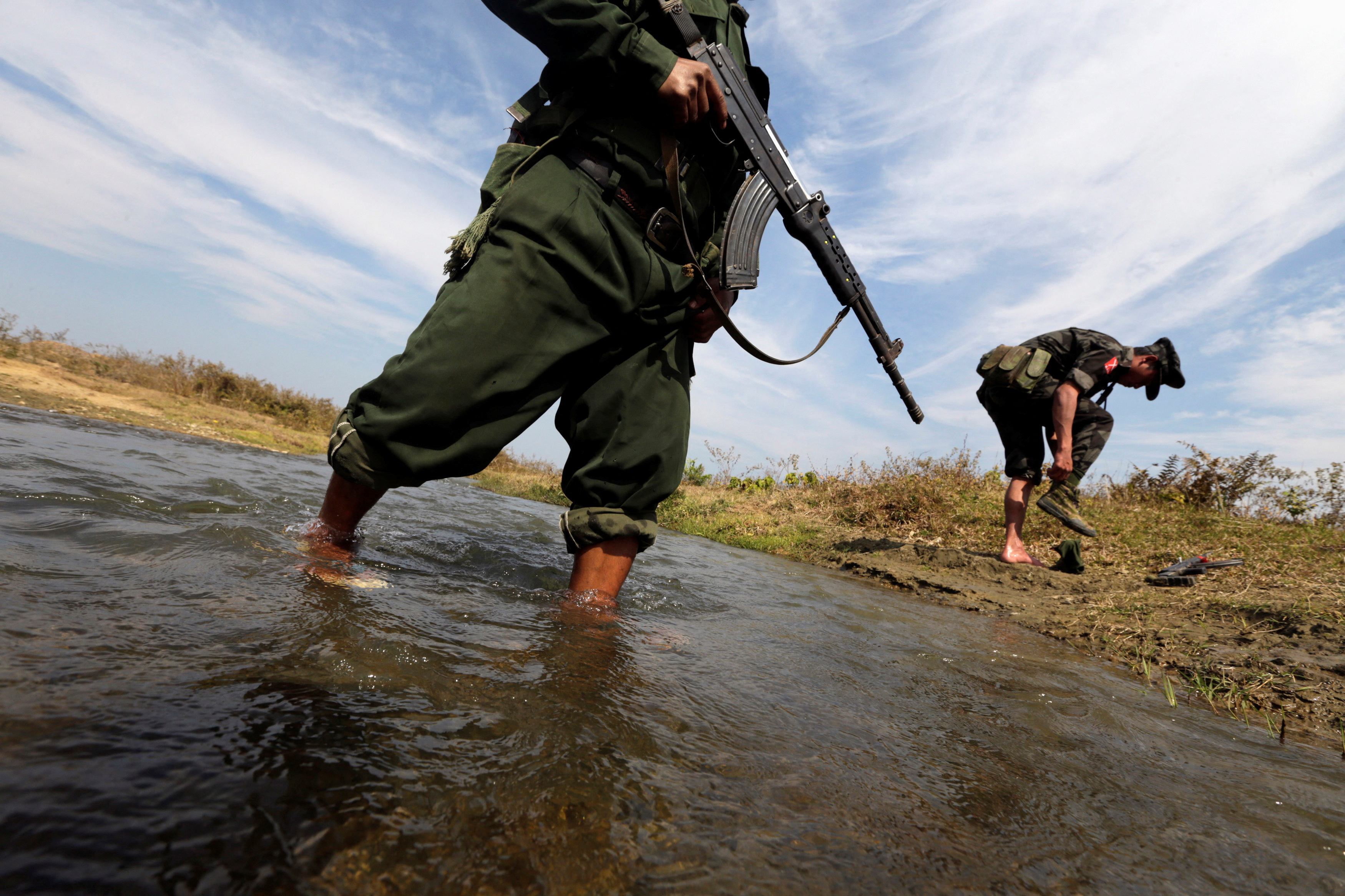 A soldier from the Kachin Independence Army puts on his shoes as he and his comrade cross a stream towards the front line in Laiza