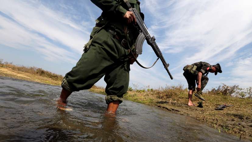 A soldier from the Kachin Independence Army puts on his shoes as he and his comrade cross a stream towards the front line in Laiza