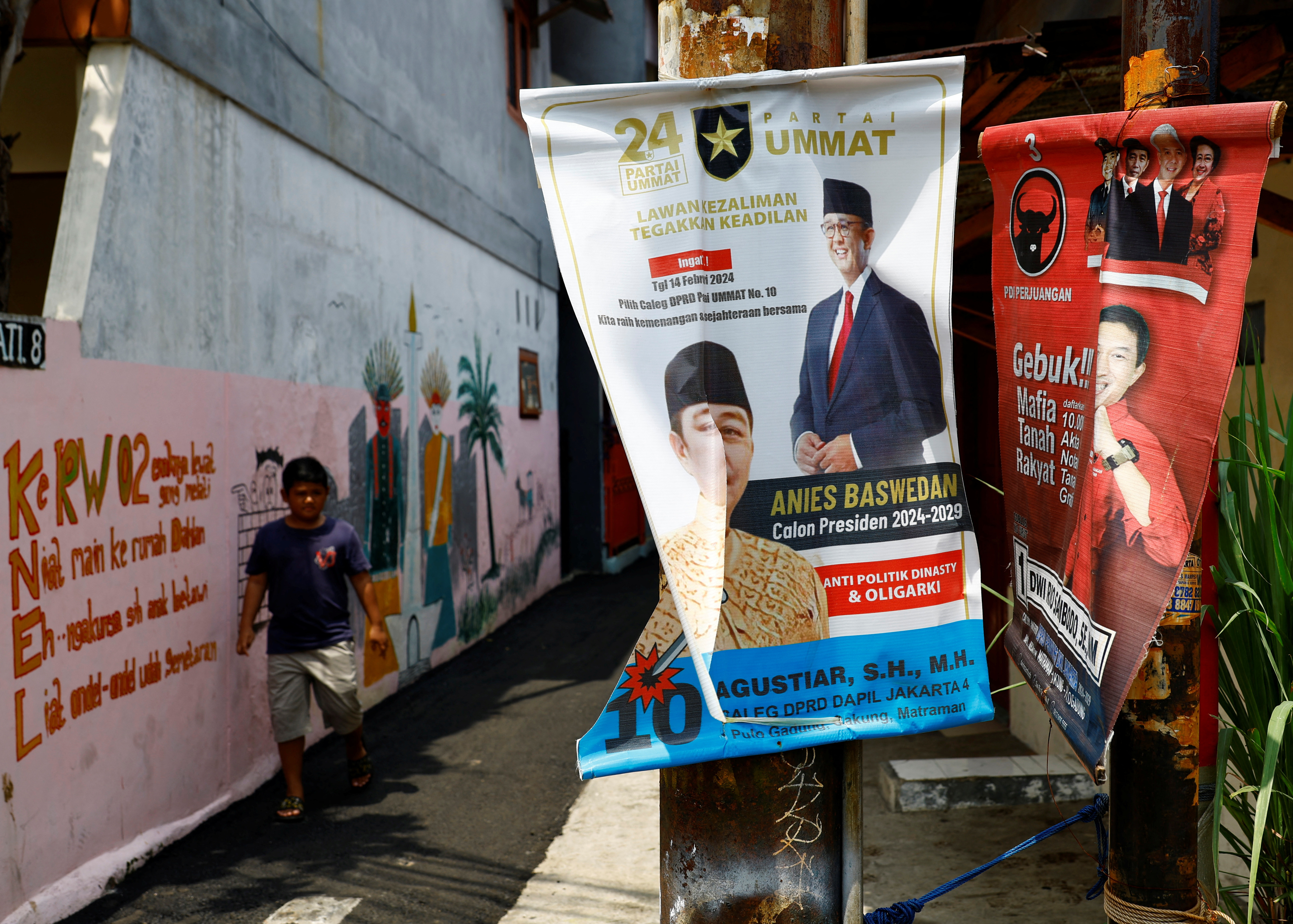 A boy walks past posters bearing the images of Presidential candidates Anies Baswedan and Ganjar Pranowo at a residential area in Jakarta