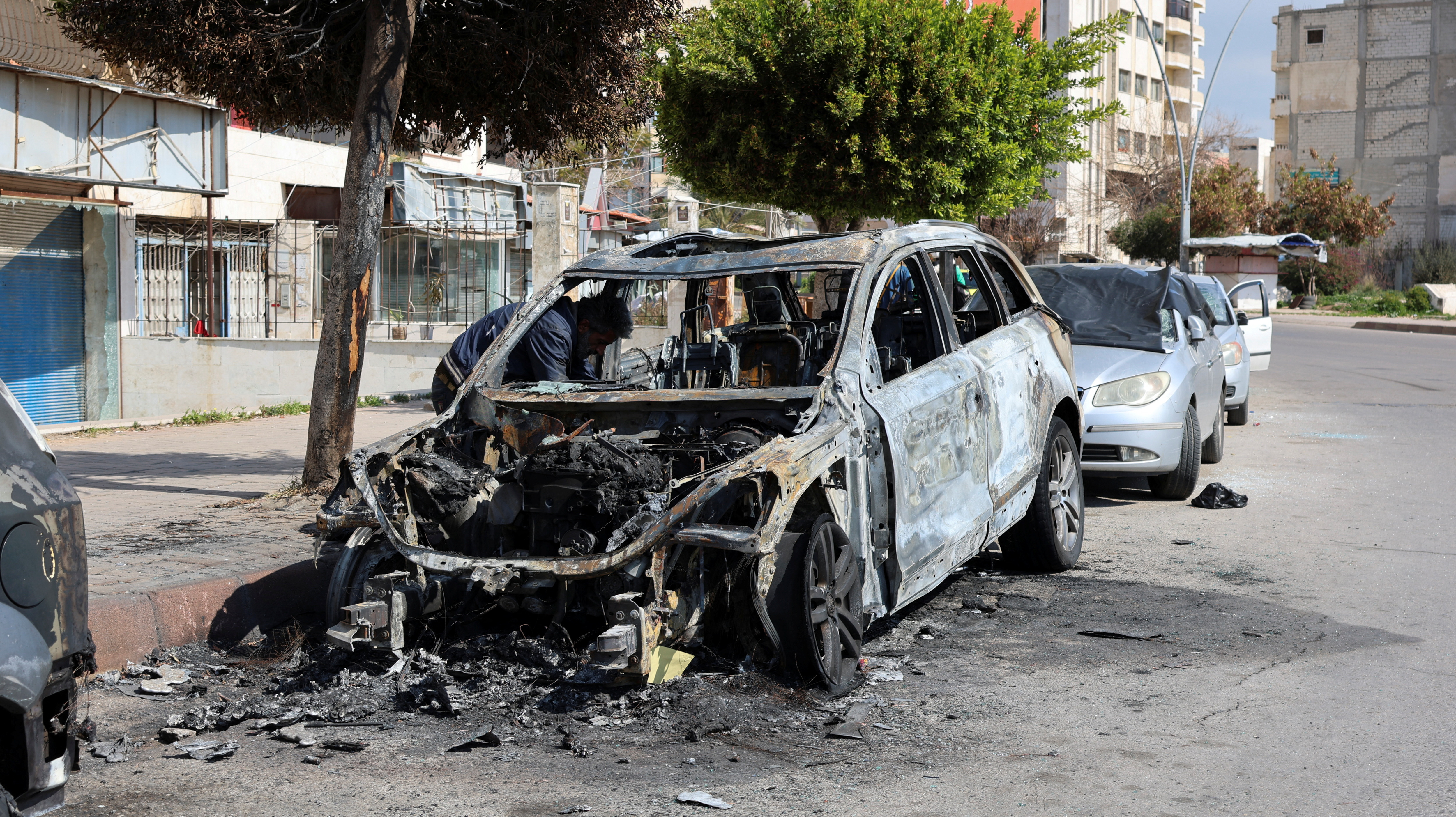 A man inspects a damaged car in Latakia