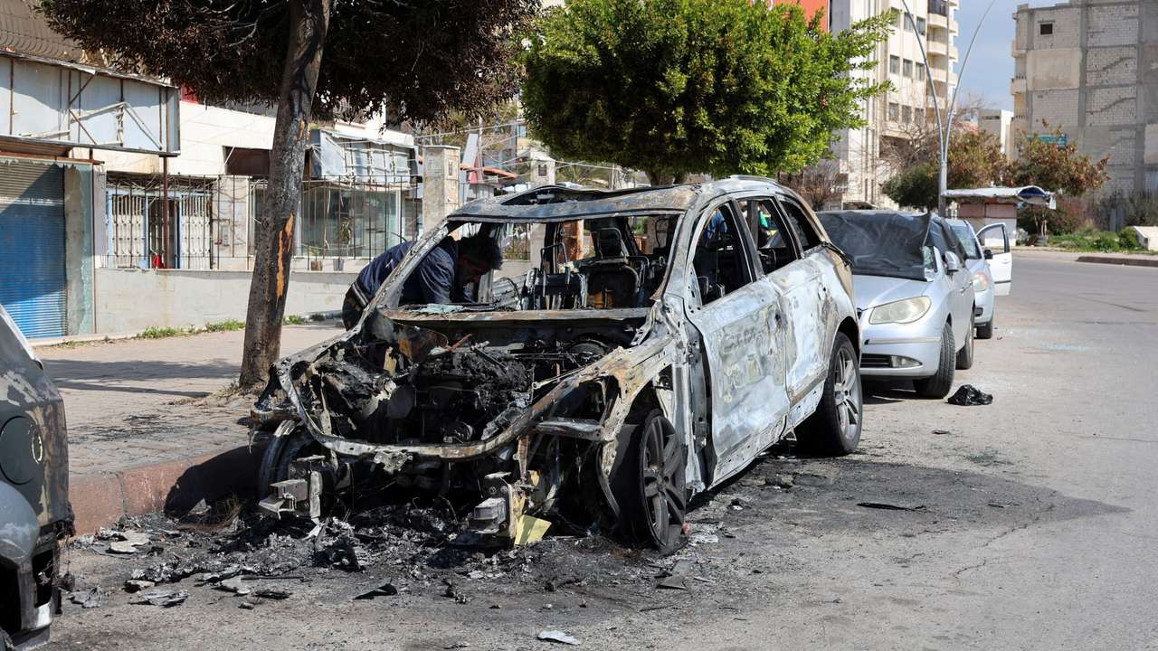 A man inspects a damaged car in Latakia