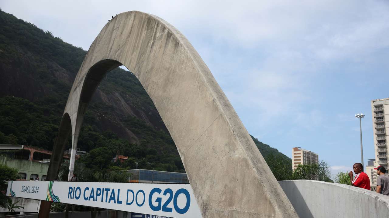 People walk next to a banner ahead of a meeting of foreign ministers, as part of Brazil's presidency of the G20 group of advanced economies, in the Rocinha slum in Rio de Janeiro