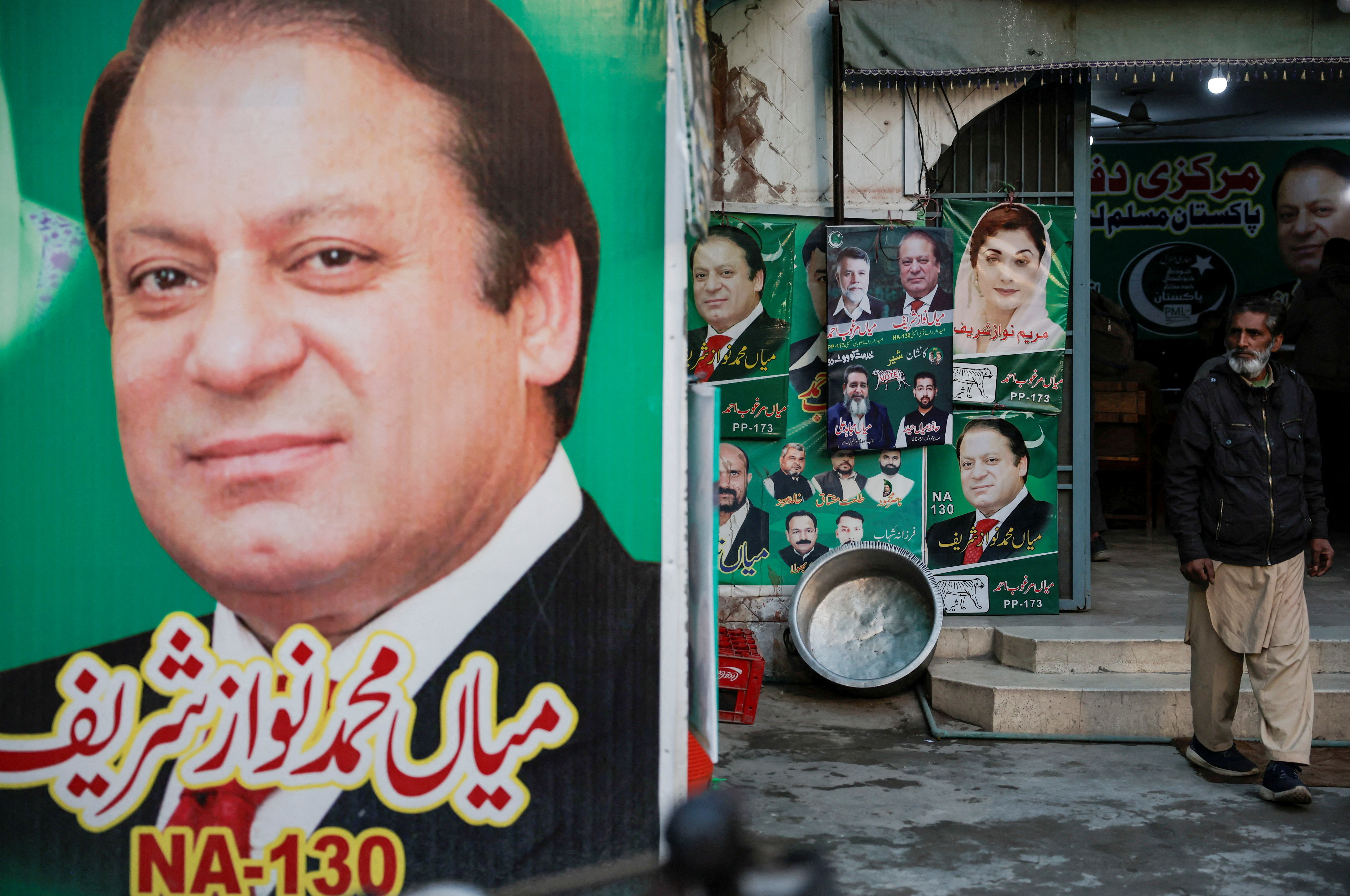 FILE PHOTO: A man stands near the banner and campaign posters of Pakistan's former Prime Minister Nawaz Sharif ahead of the general elections