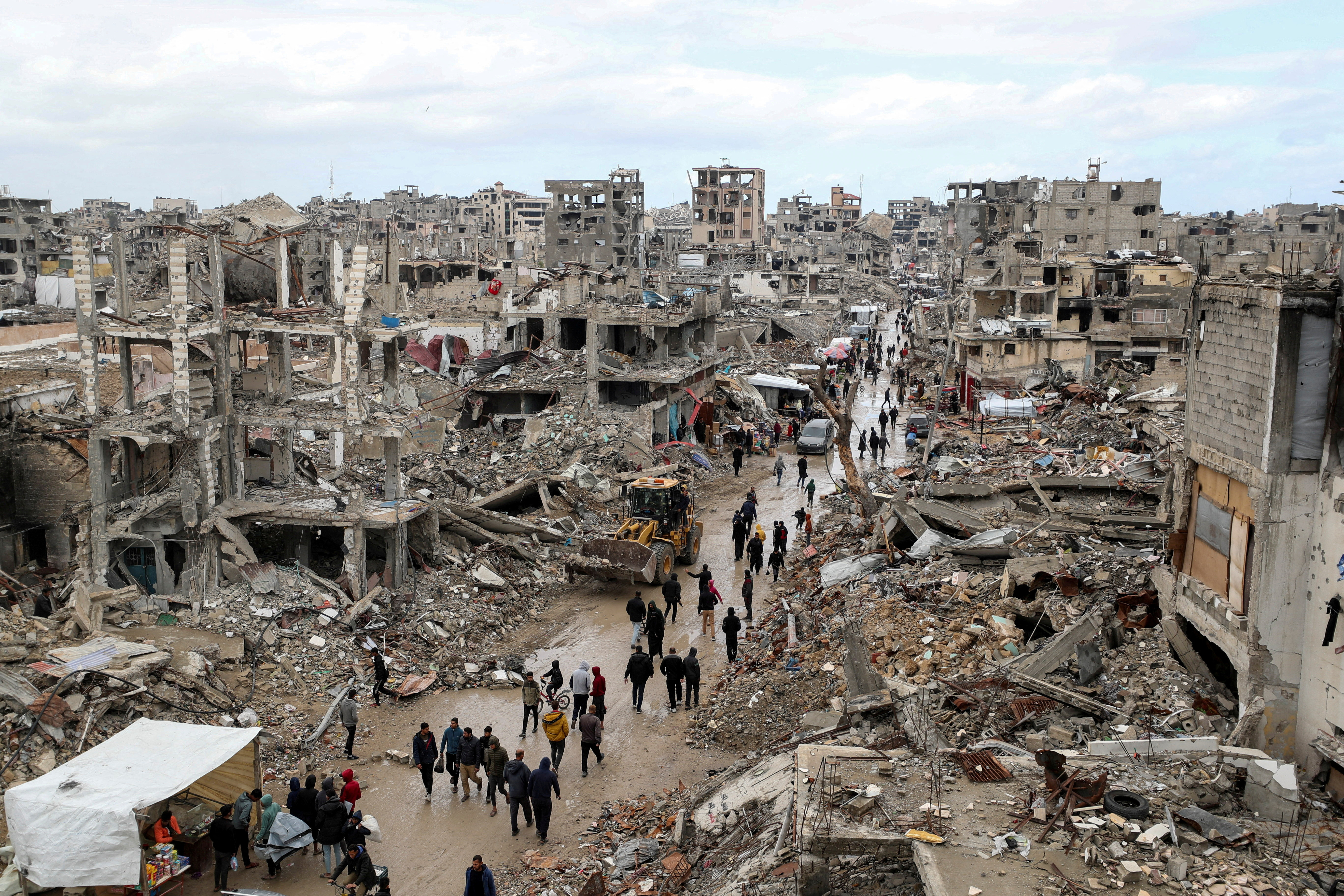 FILE PHOTO: Palestinians walk past the rubble of buildings destroyed during the Israeli offensive, on a rainy day, amid a ceasefire between Israel and Hamas, in Gaza City