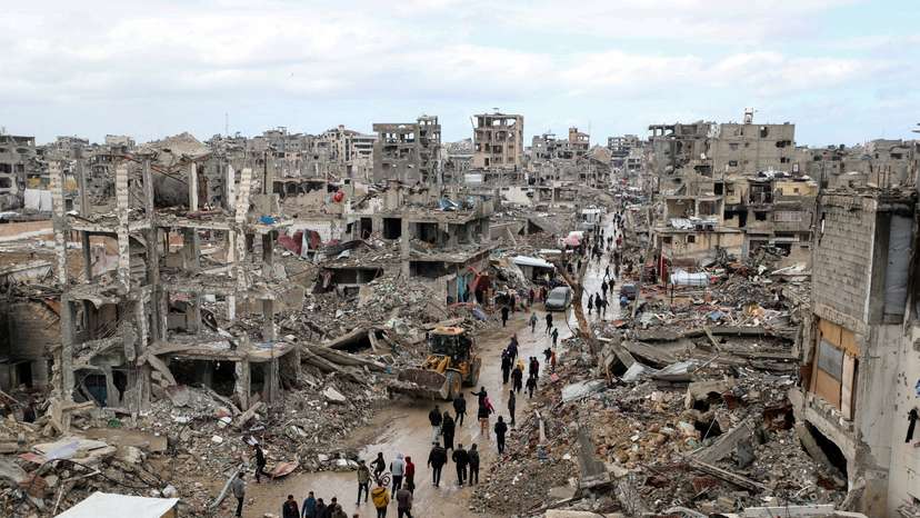 FILE PHOTO: Palestinians walk past the rubble of buildings destroyed during the Israeli offensive, on a rainy day, amid a ceasefire between Israel and Hamas, in Gaza City