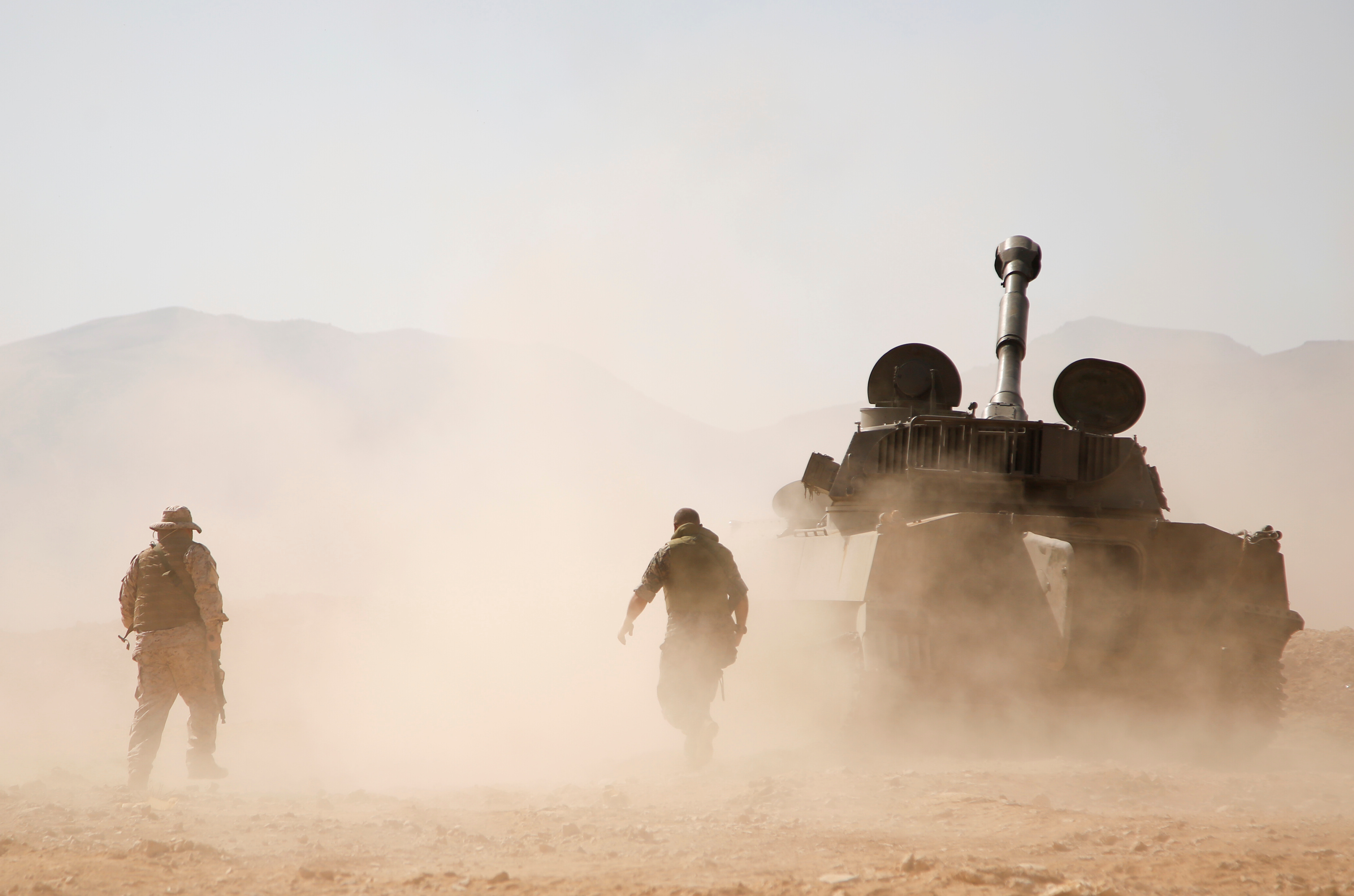 Hezbollah fighter walk near a military tank in Western Qalamoun