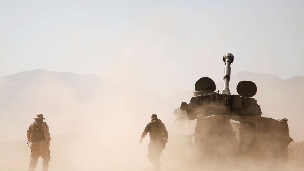 Hezbollah fighter walk near a military tank in Western Qalamoun