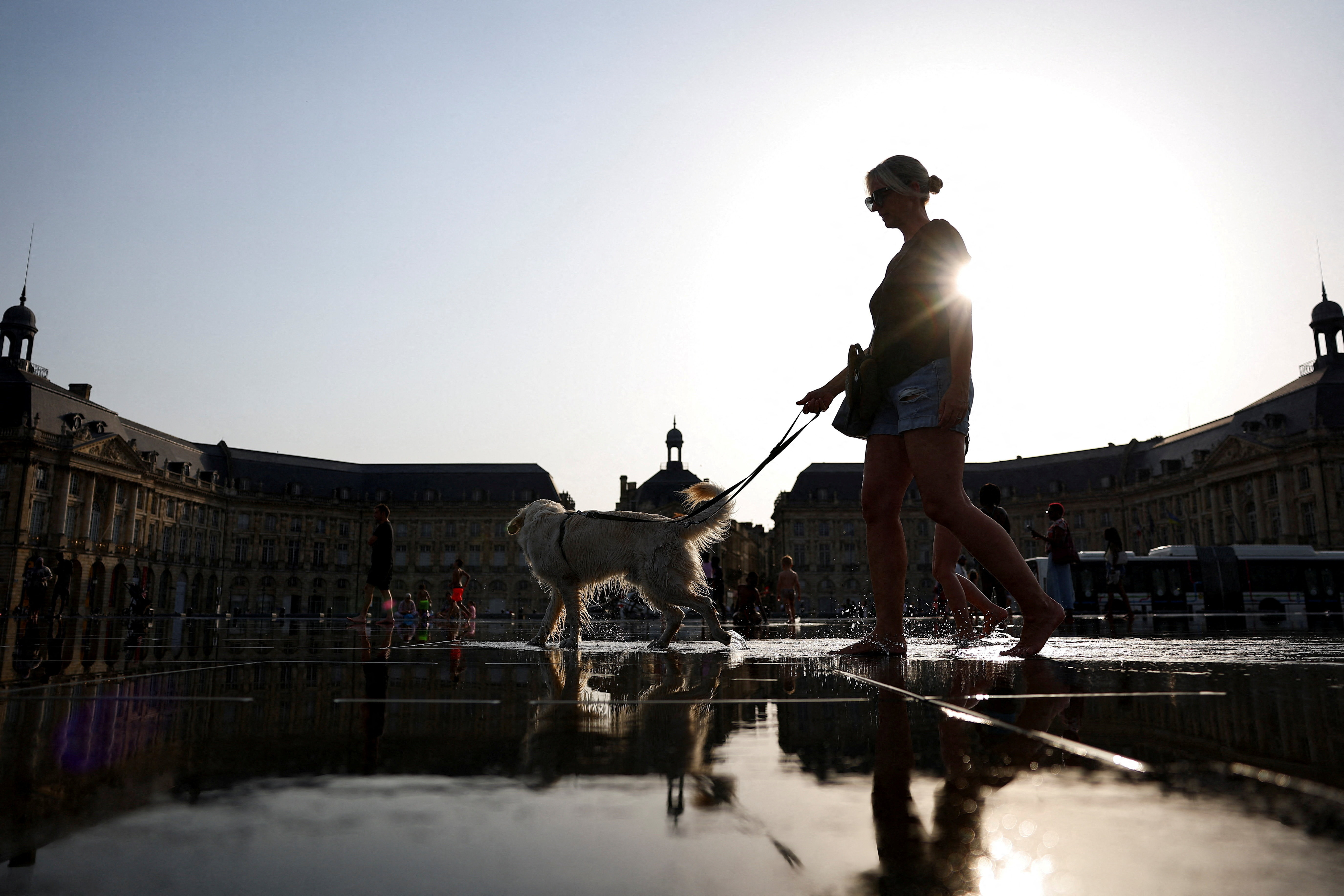 Woman walks with her dog through the shallow water of the Miroir d’eau in Bordeaux