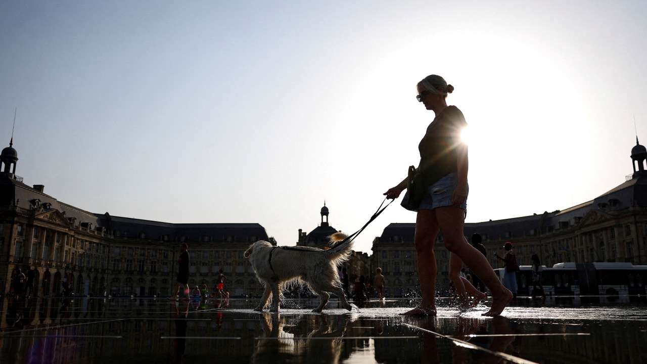 Woman walks with her dog through the shallow water of the Miroir d’eau in Bordeaux