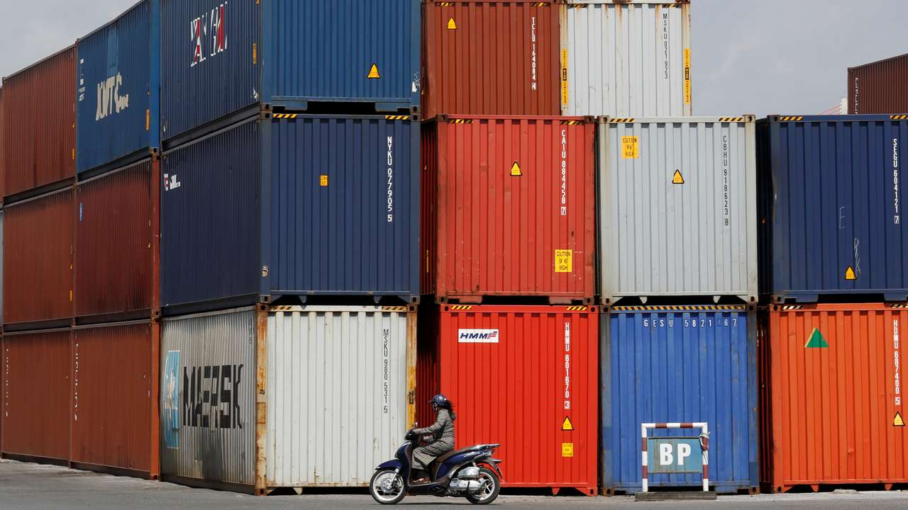 Woman rides a motorcycle as she passes containers at Hai Phong port