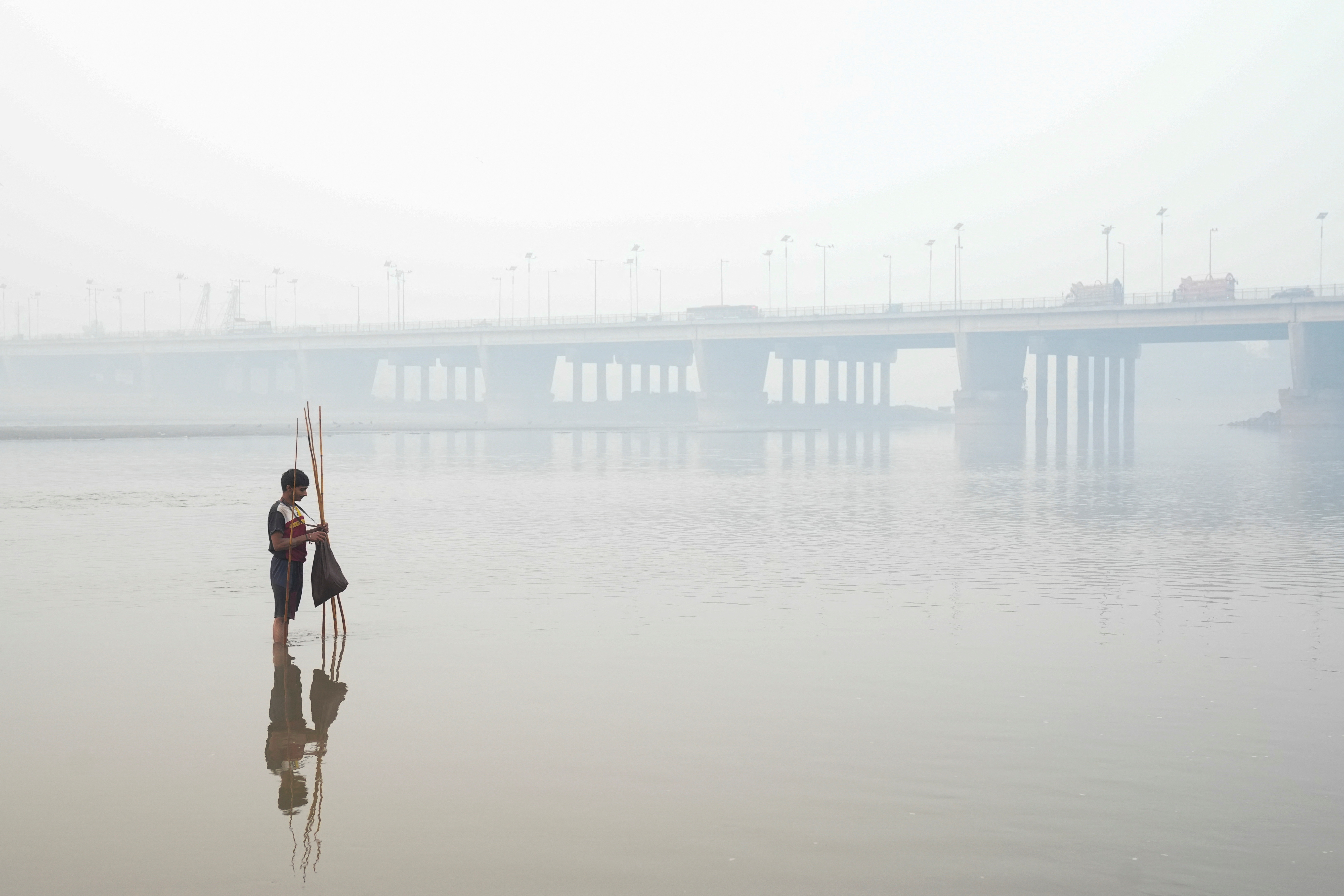 Faheem sets up a fishing trap, with the bridge over the River Ravi in the background, amid smog in Lahore