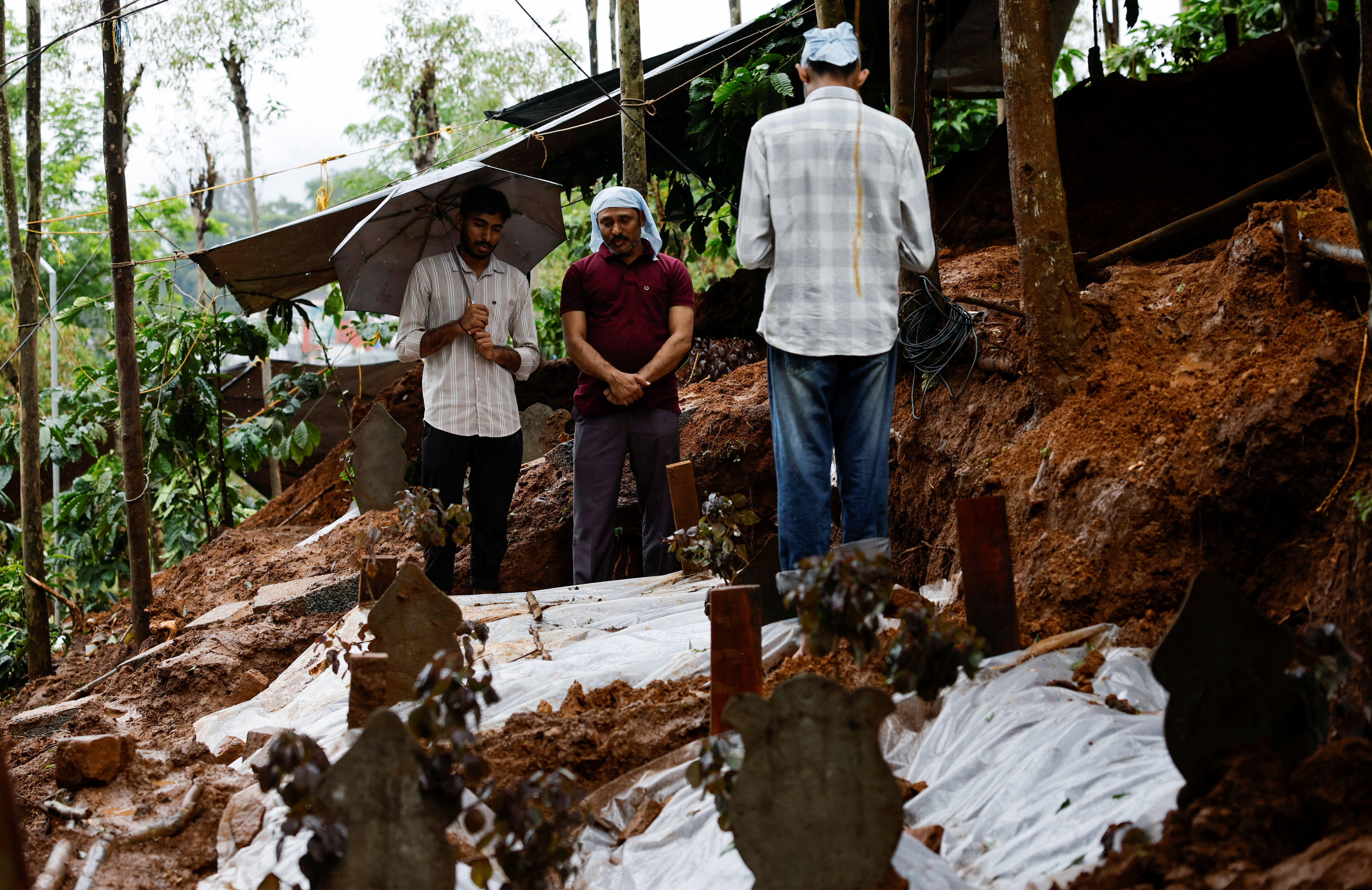 People pray for a departed family member at their grave after landslides hit several villages in Wayanad district, in Meppadi