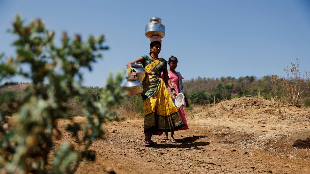 People carrying pots walk towards a well to draw water from it on a hot day in Kasara