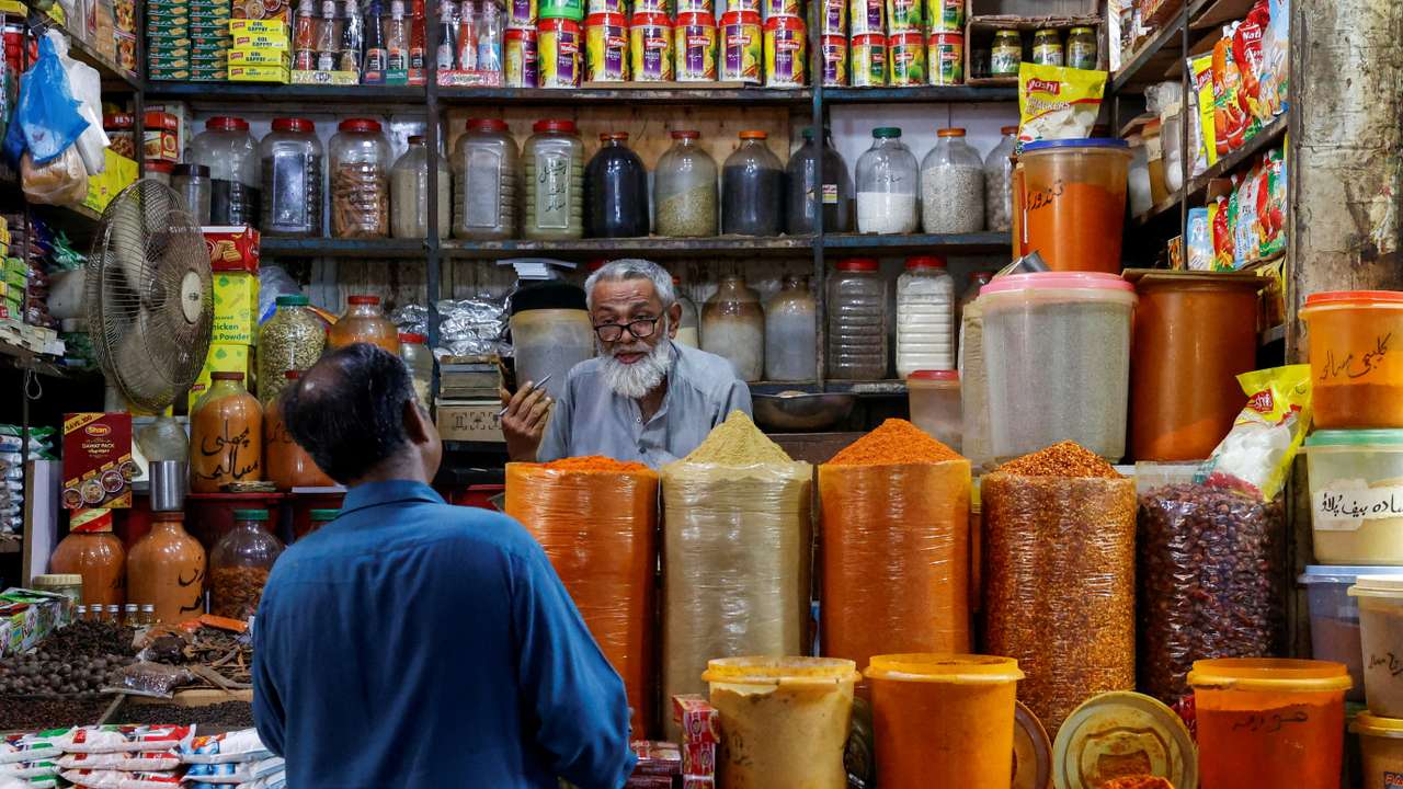 Shopkeeper speaks with a customer while selling spices at a market in Karachi