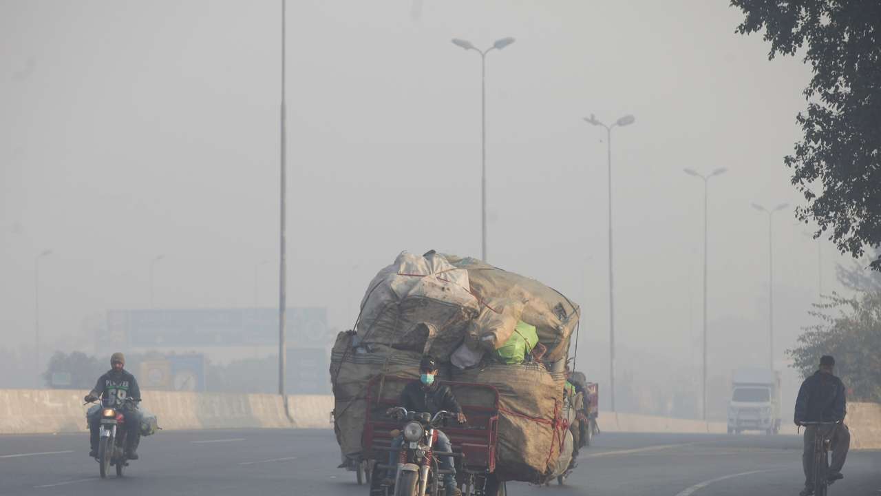 Man rides a motor tricycle, loaded with sacks of recyclables, amid dense smog in Lahore