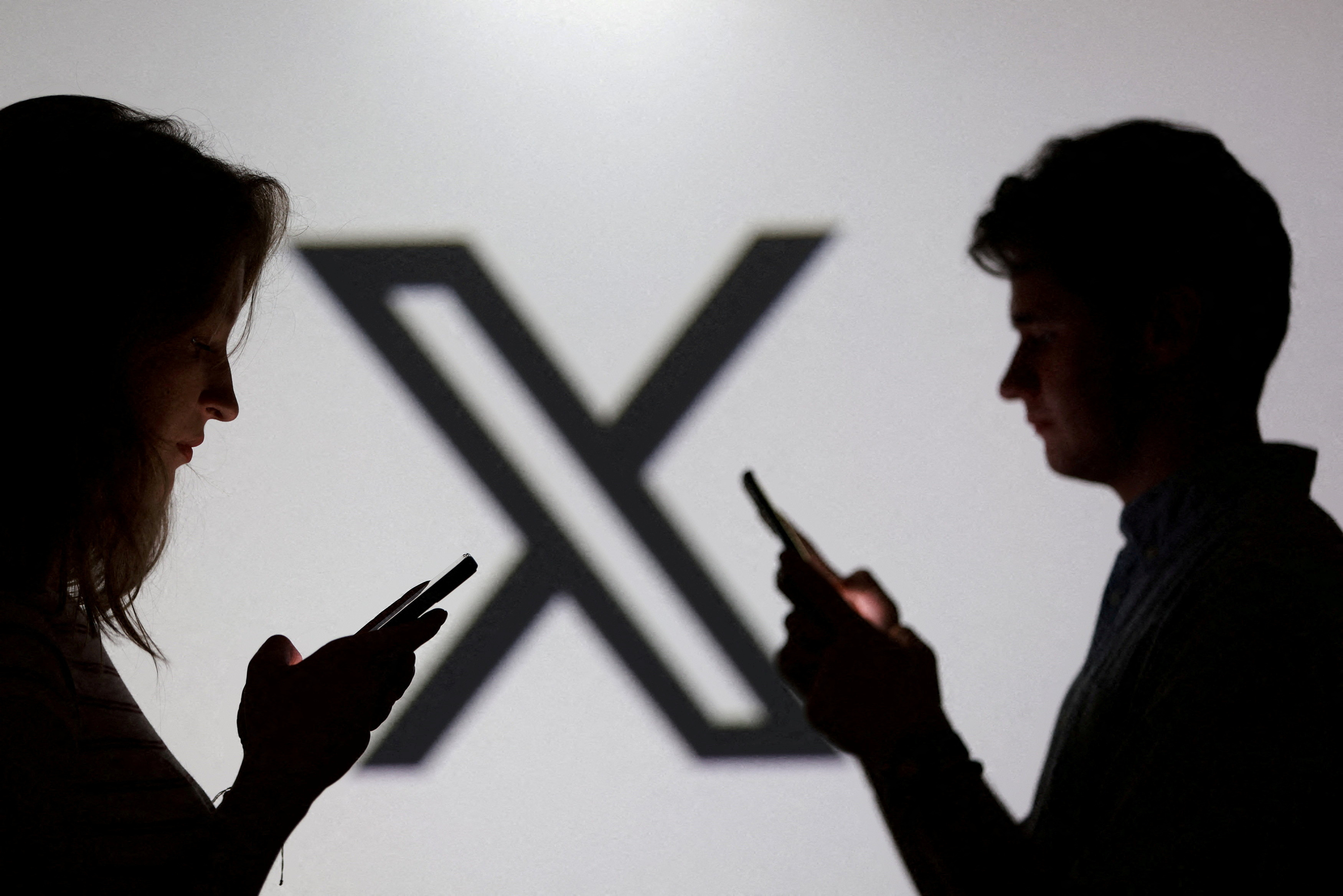 FILE PHOTO: Illustration shows teenagers pose for a photo while holding smartphones in front of a X logo