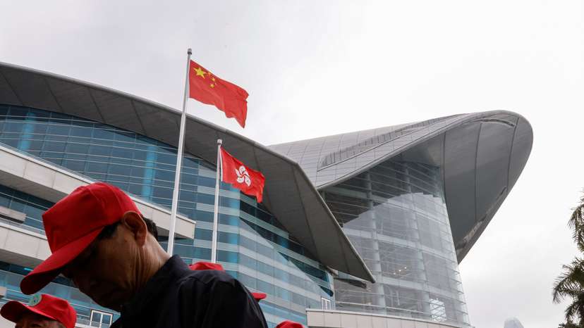 FILE PHOTO: Chinese tourists walk in front of the Chinese and Hong Kong flags, outside the Convention and Exhibition Centre, in Hong Kong