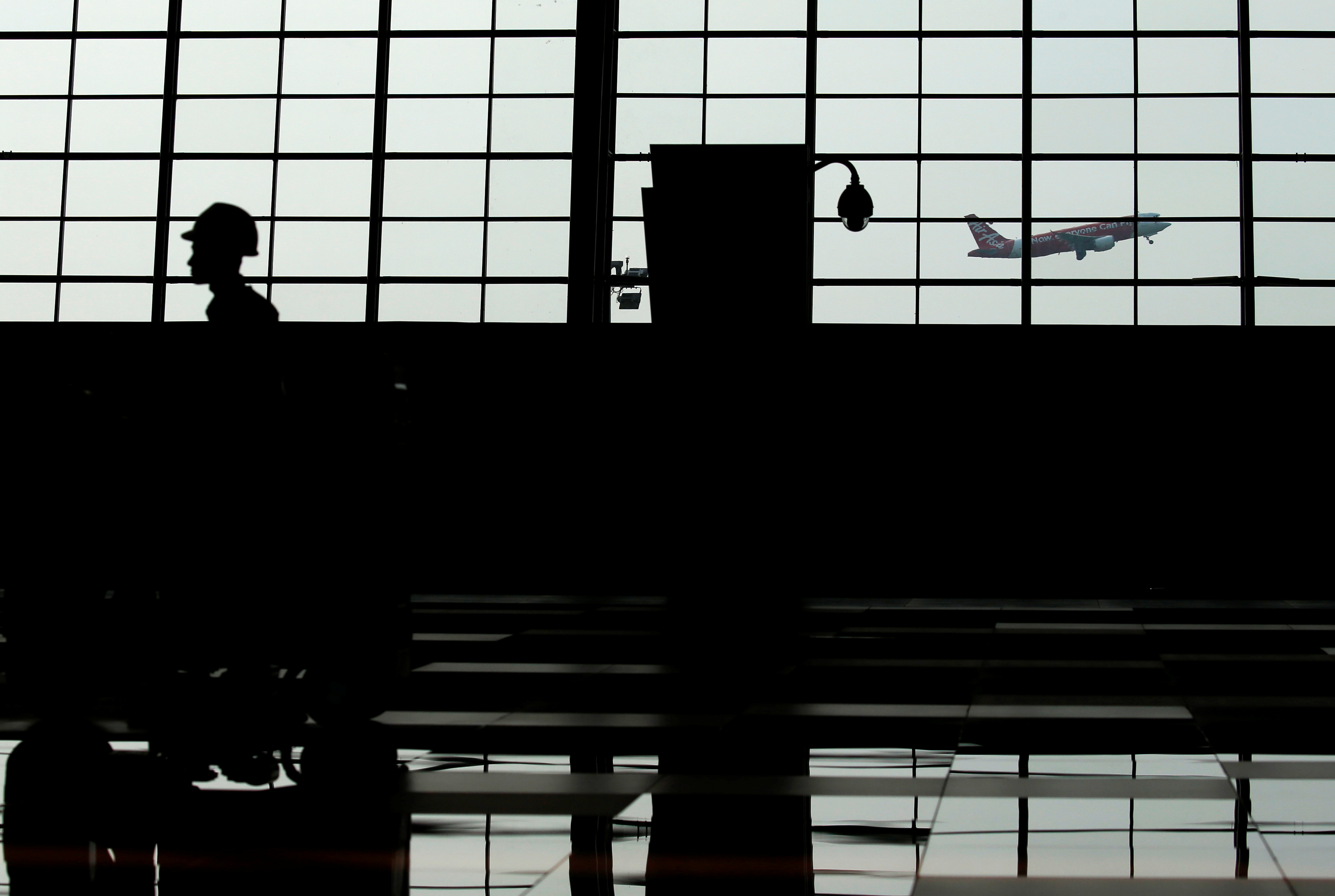 A worker cleans the floor as an AirAsia plane is seen flying past the new Terminal 3 Ultimate at Soekarno Hatta airport in Jakarta
