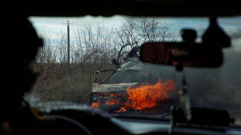 FILE PHOTO: Ukrainian servicemen move past a burning car hit by a kamikaze drone outside the front line town of Avdiivka