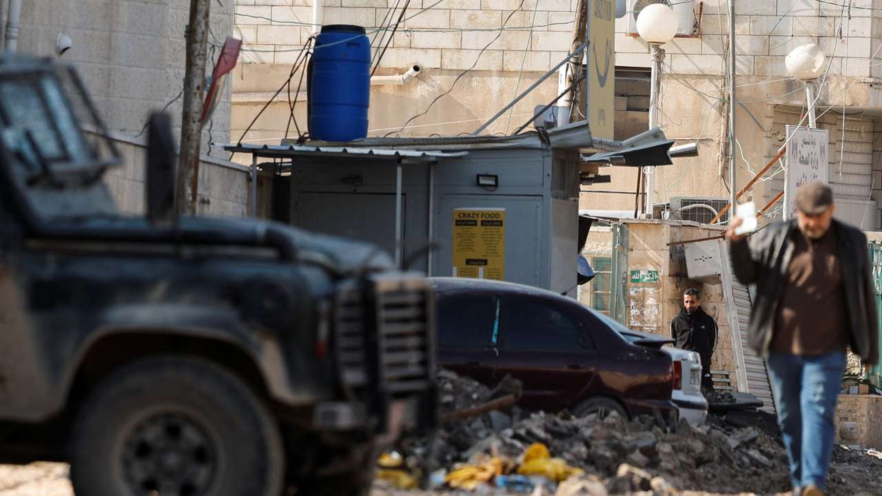 A man walks next to an Israeli military vehicle, in Jenin