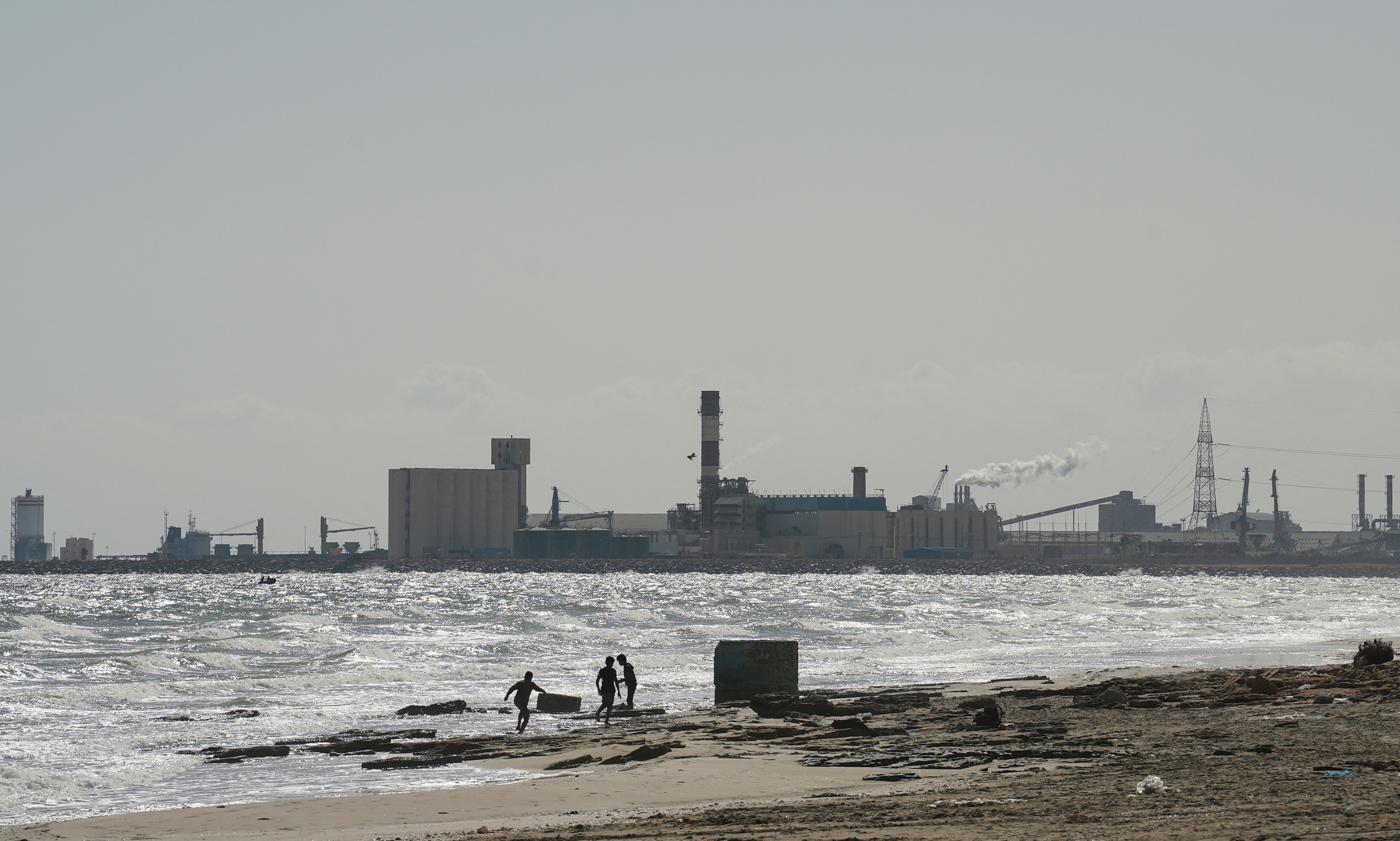 Children play on the beach with the Tunisian Chemical Group’s (CGT) phosphate complex visible in the background, in Gabes