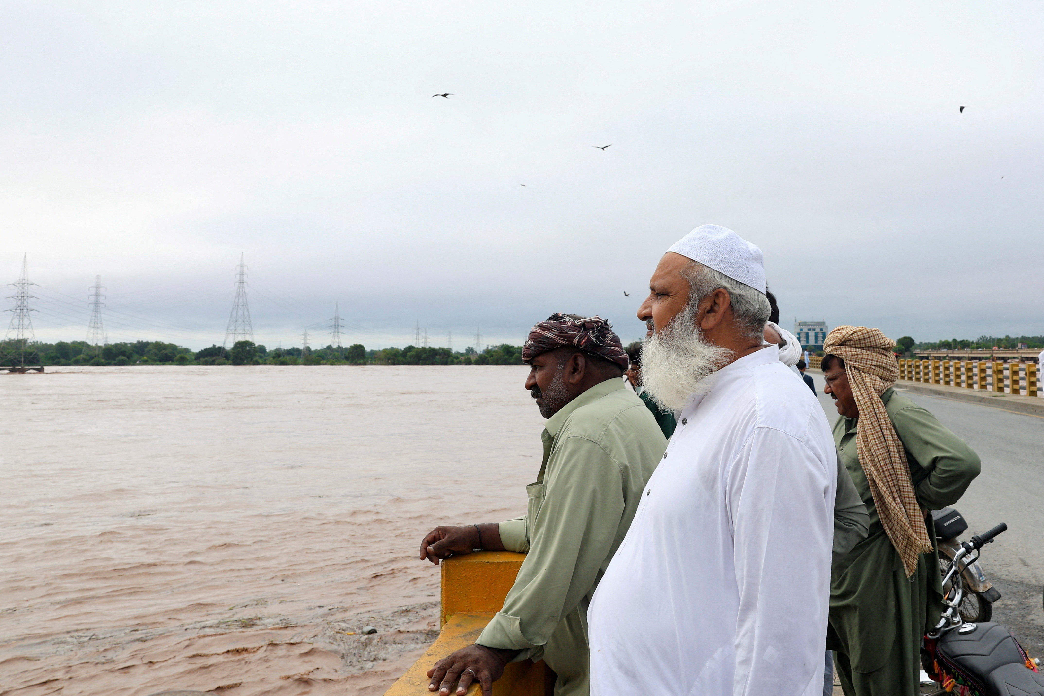 Men stand on a bridge over the Chenab River, following the monsoon rains and rising water level in Wazirabad