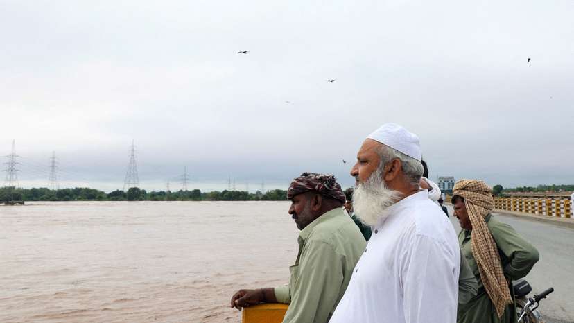 Men stand on a bridge over the Chenab River, following the monsoon rains and rising water level in Wazirabad
