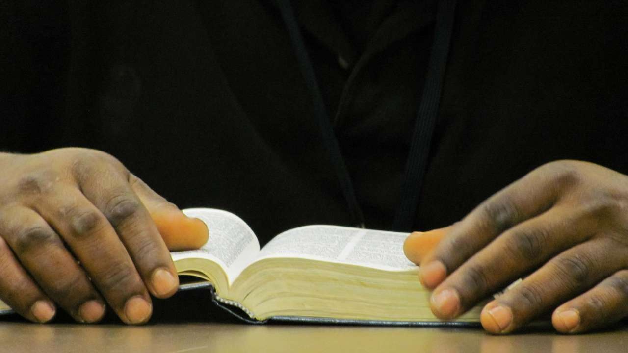 Imagem mostra mãos segurando livro aberto sobre mesa