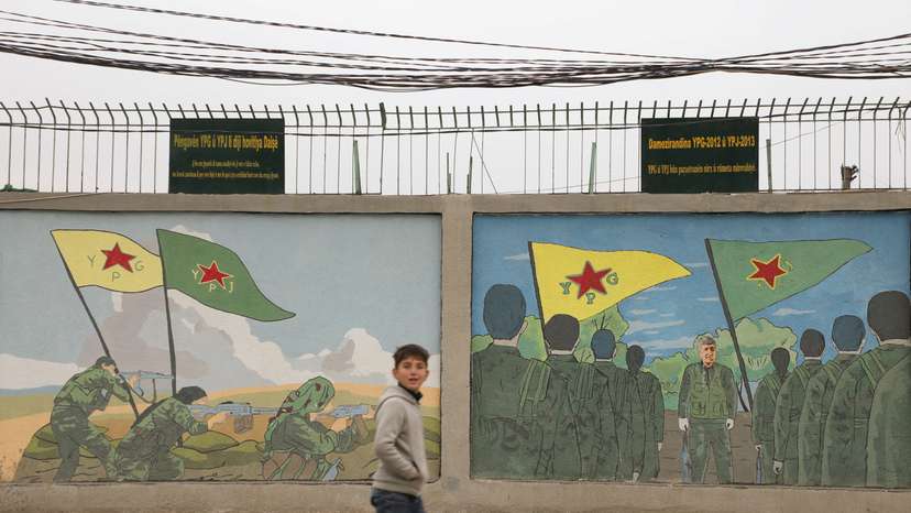 A boy walks past drawings on a wall depicting Kurdish People's Protection Units (YPG) and Kurdish female fighters of the Women's Protection Unit (YPJ) flags in Qamishli