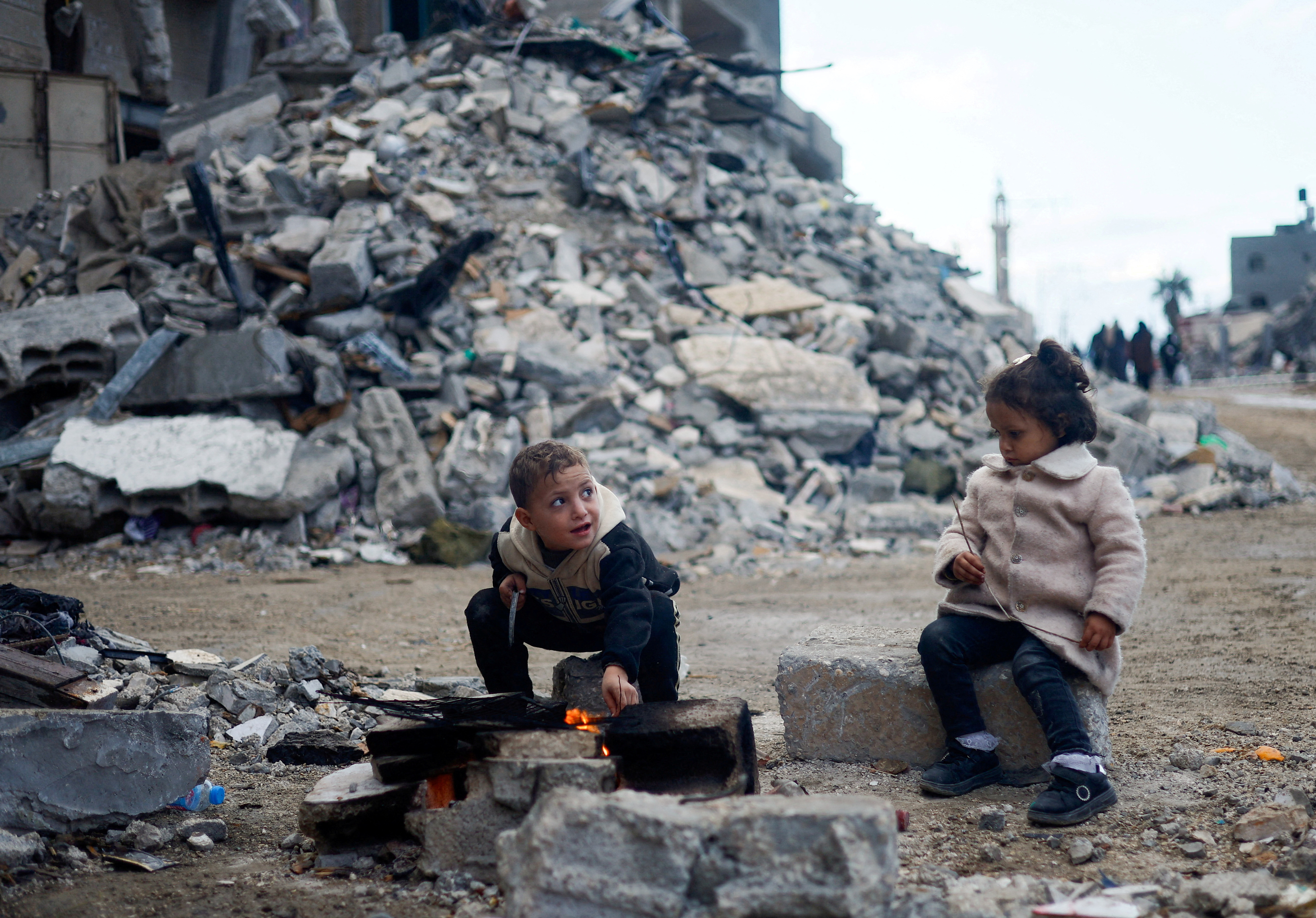 Palestinian children sit by the fire next to the rubble of a house, in Khan Younis