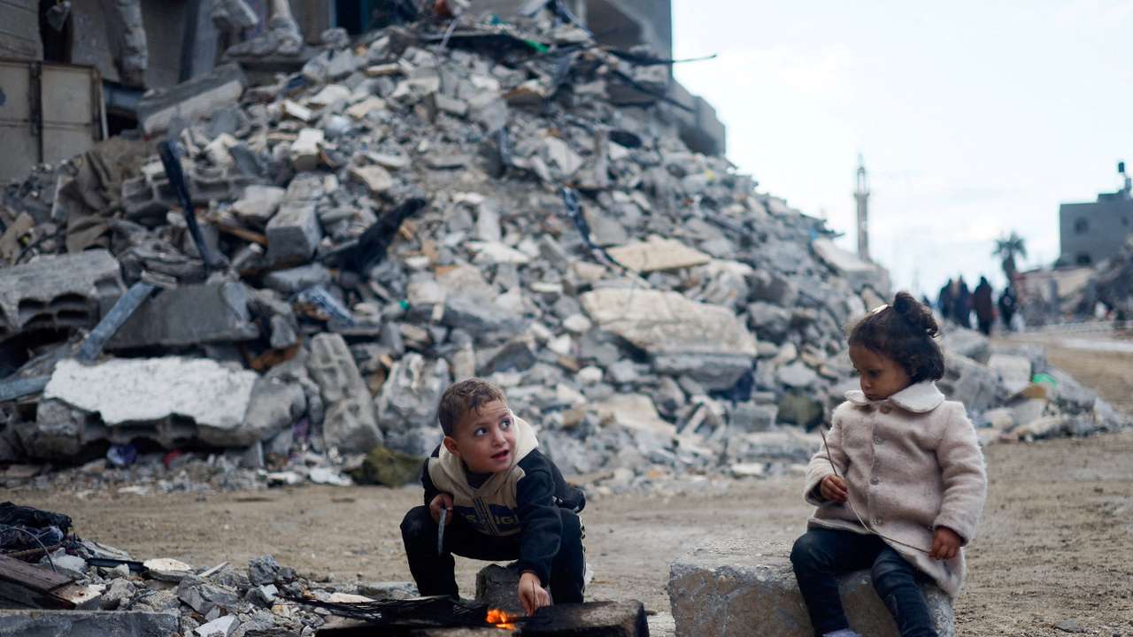 Palestinian children sit by the fire next to the rubble of a house, in Khan Younis