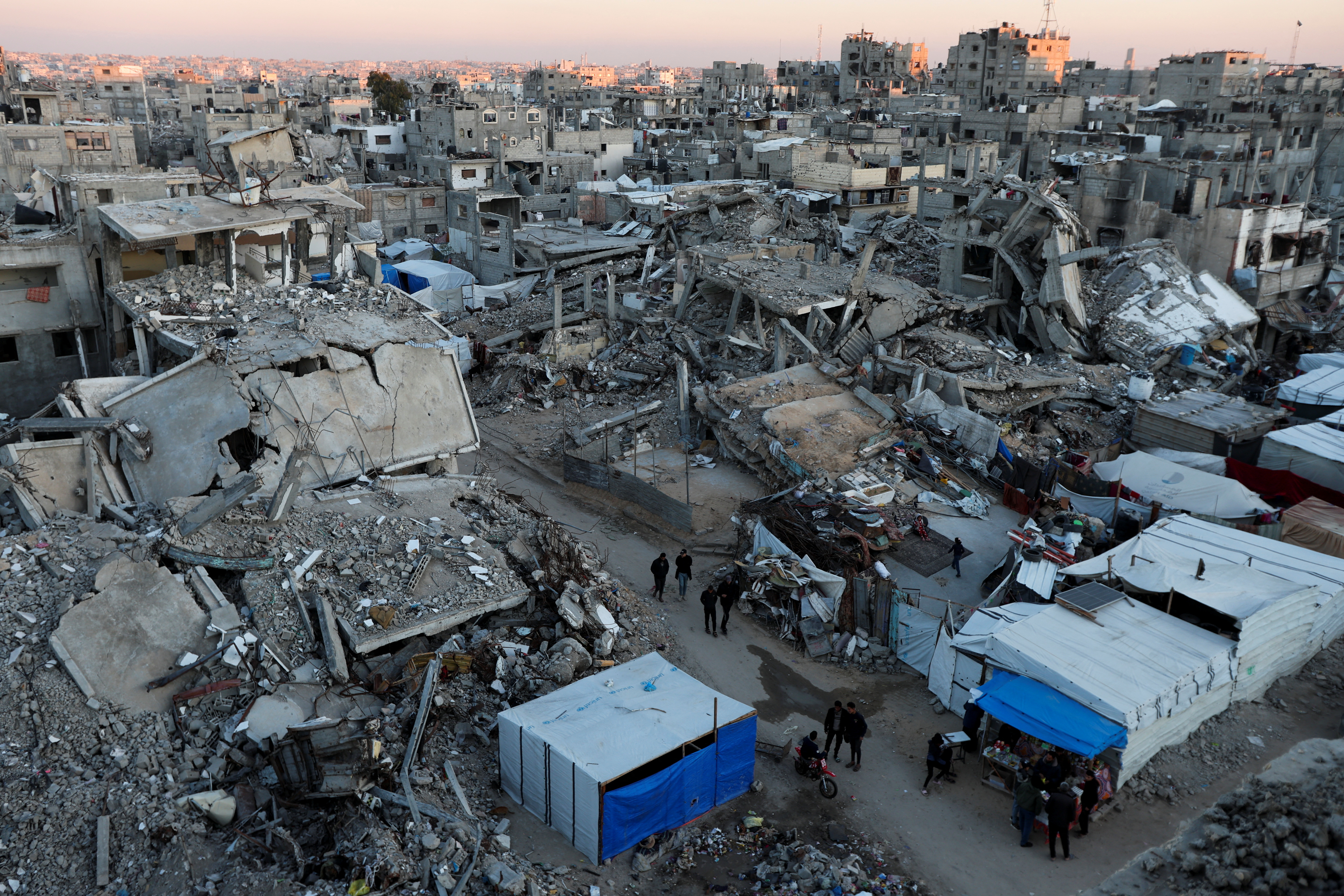 Palestinians walk past the rubble of buildings, In Khan Younis